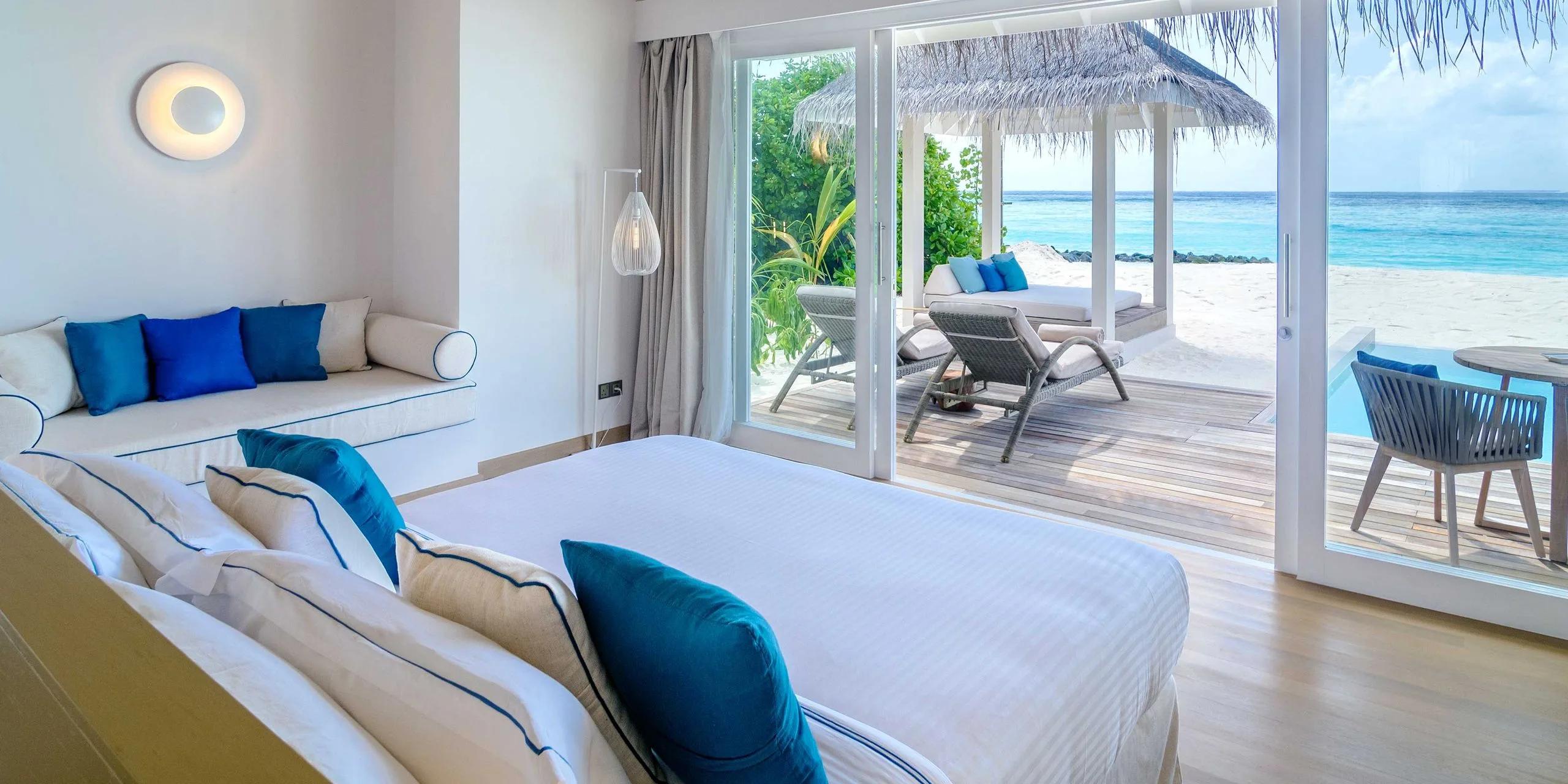 A Deluxe Beach Villa with Pool's bedroom opening onto its private pool, sun loungers and a beach pavilion beyond