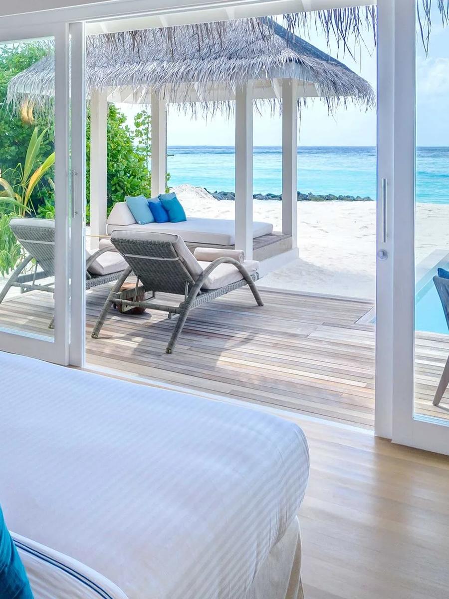 A Deluxe Beach Villa with Pool's bedroom opening onto its private pool, sun loungers and a beach pavilion beyond