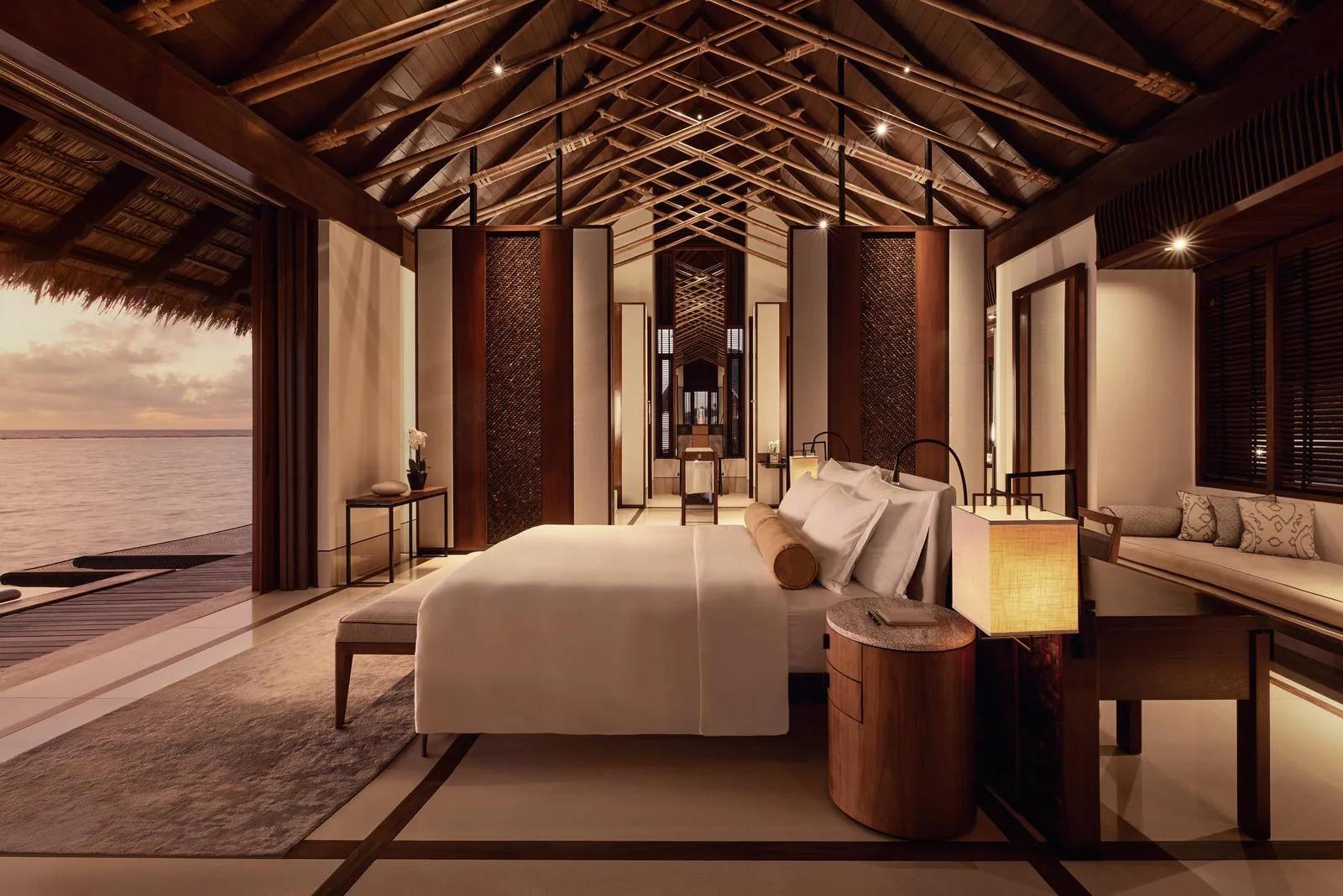 The bedroom of a Water Villa with Pool at One&Only Reethi Rah, glass walls opening onto the lagoon at sunset