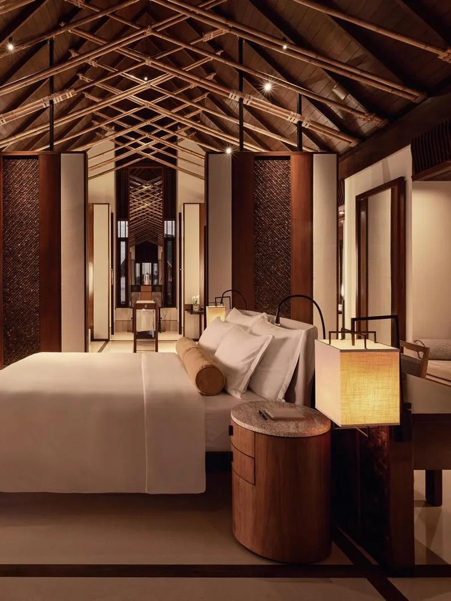 The bedroom of a Water Villa with Pool at One&Only Reethi Rah, glass walls opening onto the lagoon at sunset