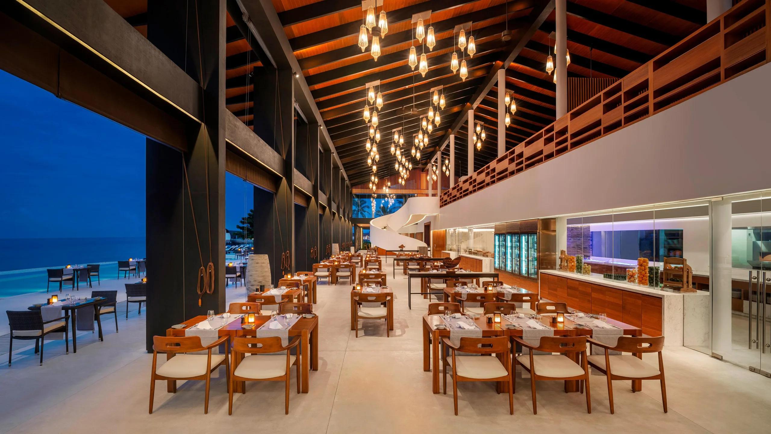 Island Kitchen's open-air dining hall in the evening, tables set beside the show kitchen with the pool visible beyond