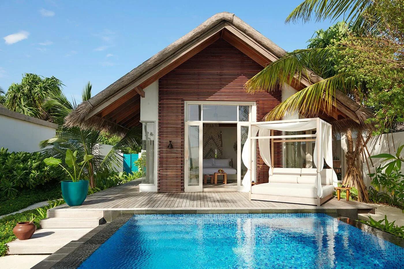 Exterior of a large beach villa with private pool and canopied daybed, set among palm trees