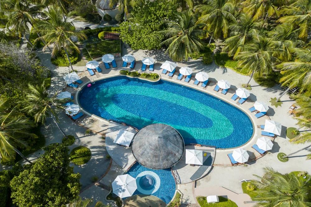 Bandos's main swimming pool from above, an oval shape ringed by loungers, umbrellas and palm trees