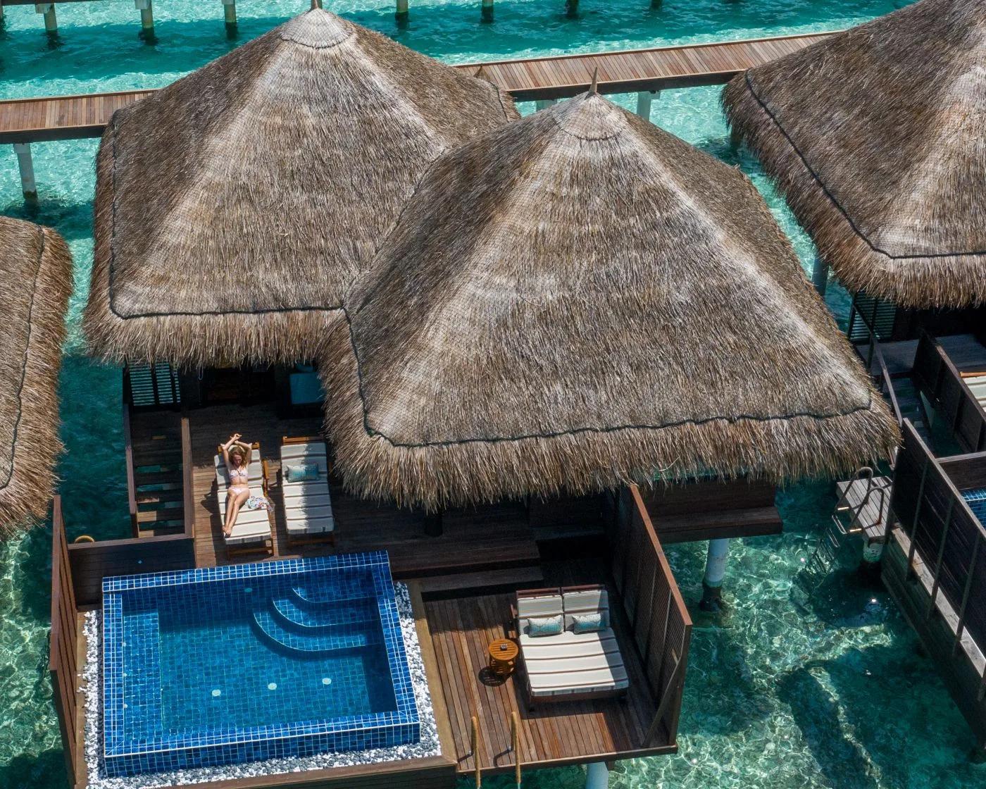 An aerial view of Overwater Villa with Pool units, turquoise lagoon surrounding the private deck pools where a guest sunbathes
