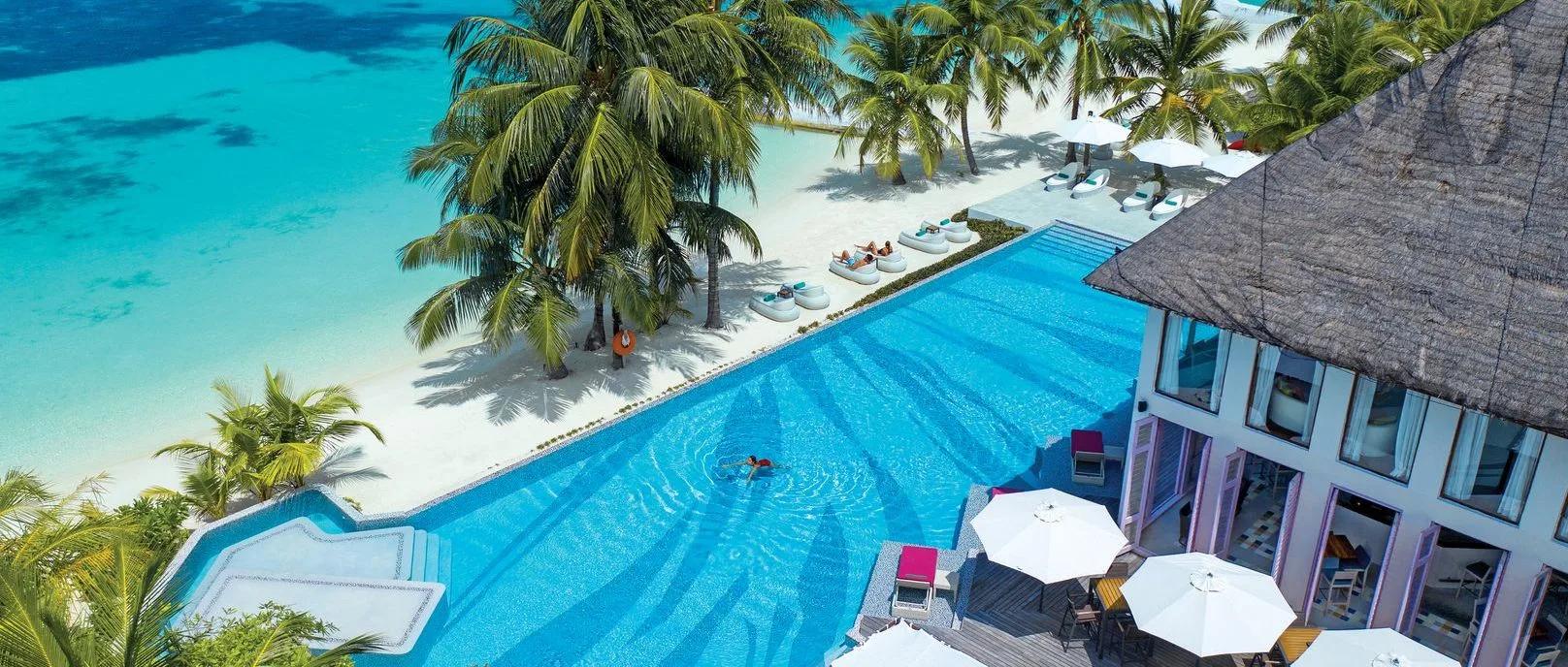 Aerial view of the lagoon-view pool beside the beach, sunbeds and a thatched pavilion at its edge