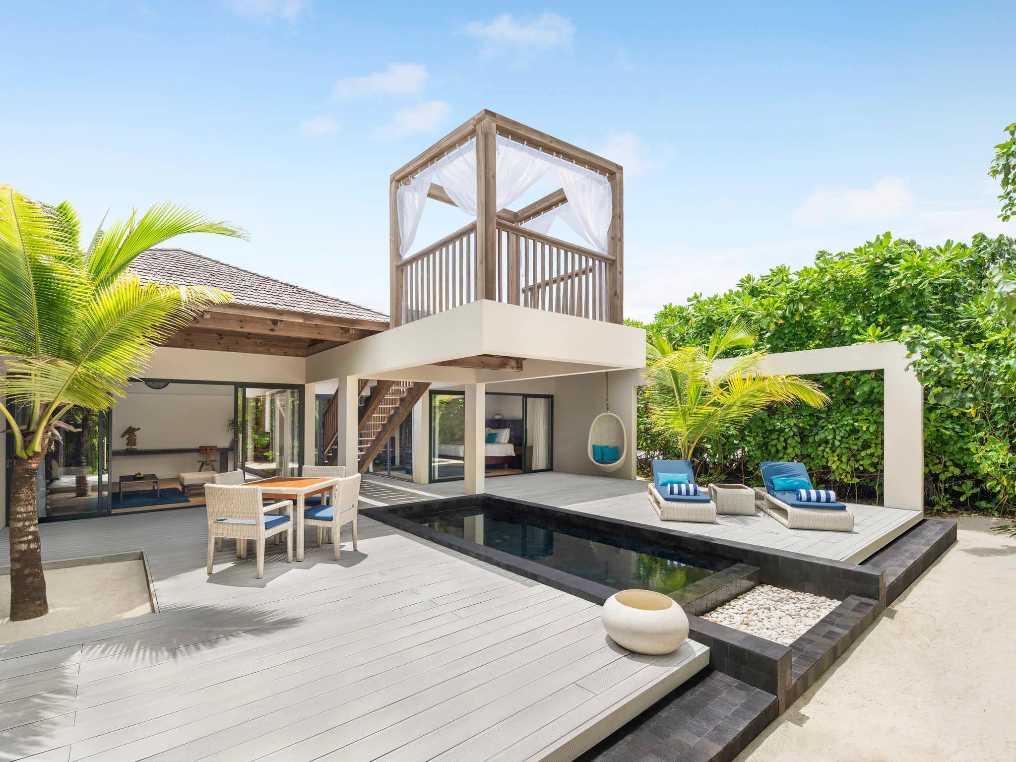 Exterior of a beach pool villa with a private plunge pool, dining table and an elevated open-air daybed loft under a thatched canopy