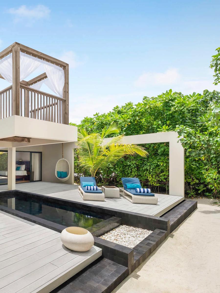 Exterior of a beach pool villa with a private plunge pool, dining table and an elevated open-air daybed loft under a thatched canopy