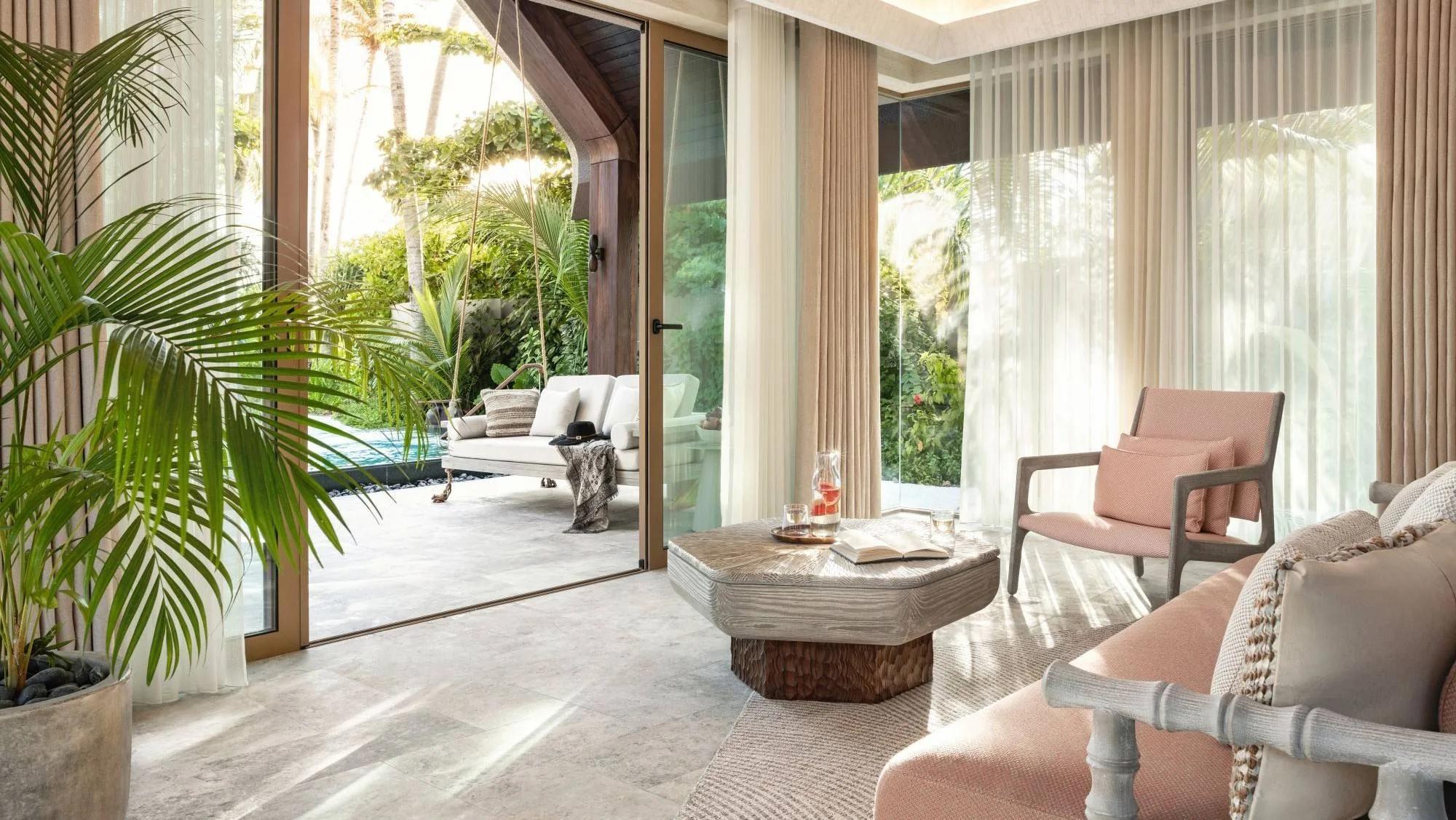The garden-facing lounge inside a Beach Pool Villa at Joali Being, glass doors open to the pool and tropical garden