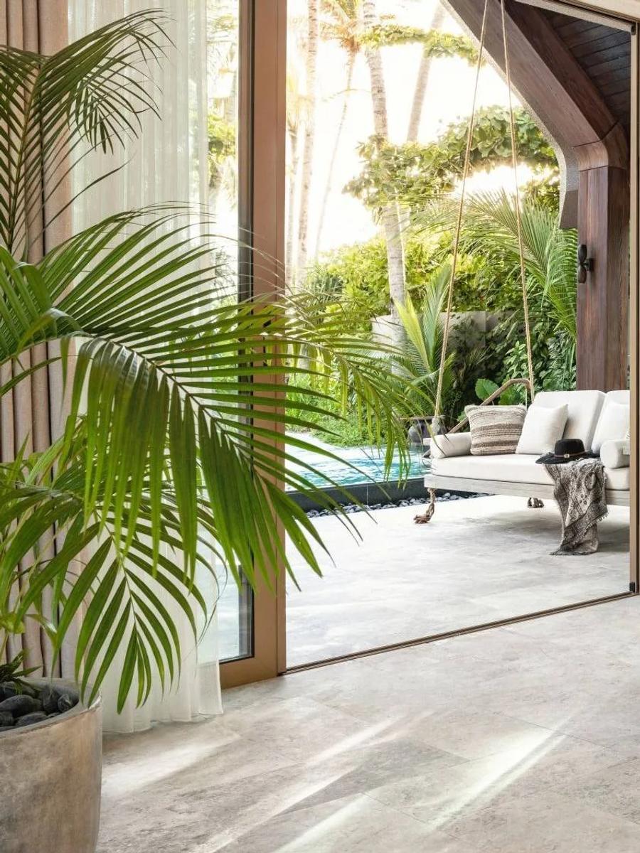 The garden-facing lounge inside a Beach Pool Villa at Joali Being, glass doors open to the pool and tropical garden