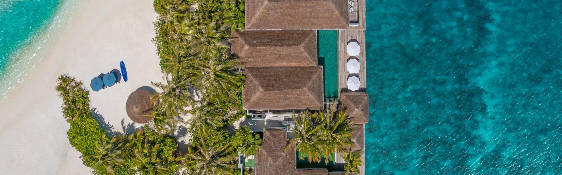 Aerial view of the two-storey Two-Bedroom Beach Pool Residence at the island's point, its multi-pitched thatched roof beside the reef-edge pool