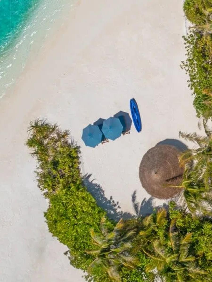 Aerial view of the two-storey Two-Bedroom Beach Pool Residence at the island's point, its multi-pitched thatched roof beside the reef-edge pool