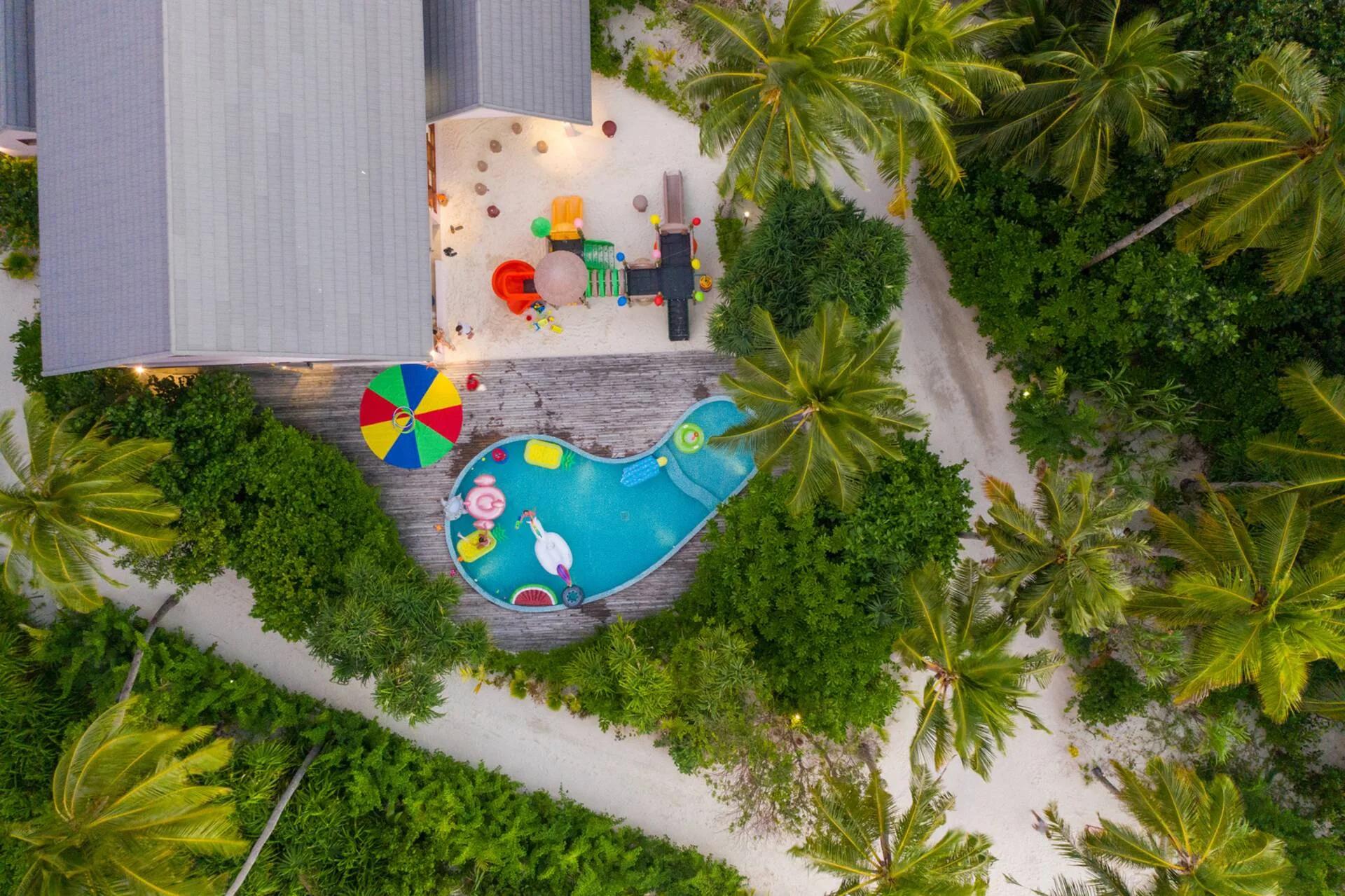 Aerial view of Lil' Shark Kids Club's whale-shaped splash pool and playground, set among palm trees