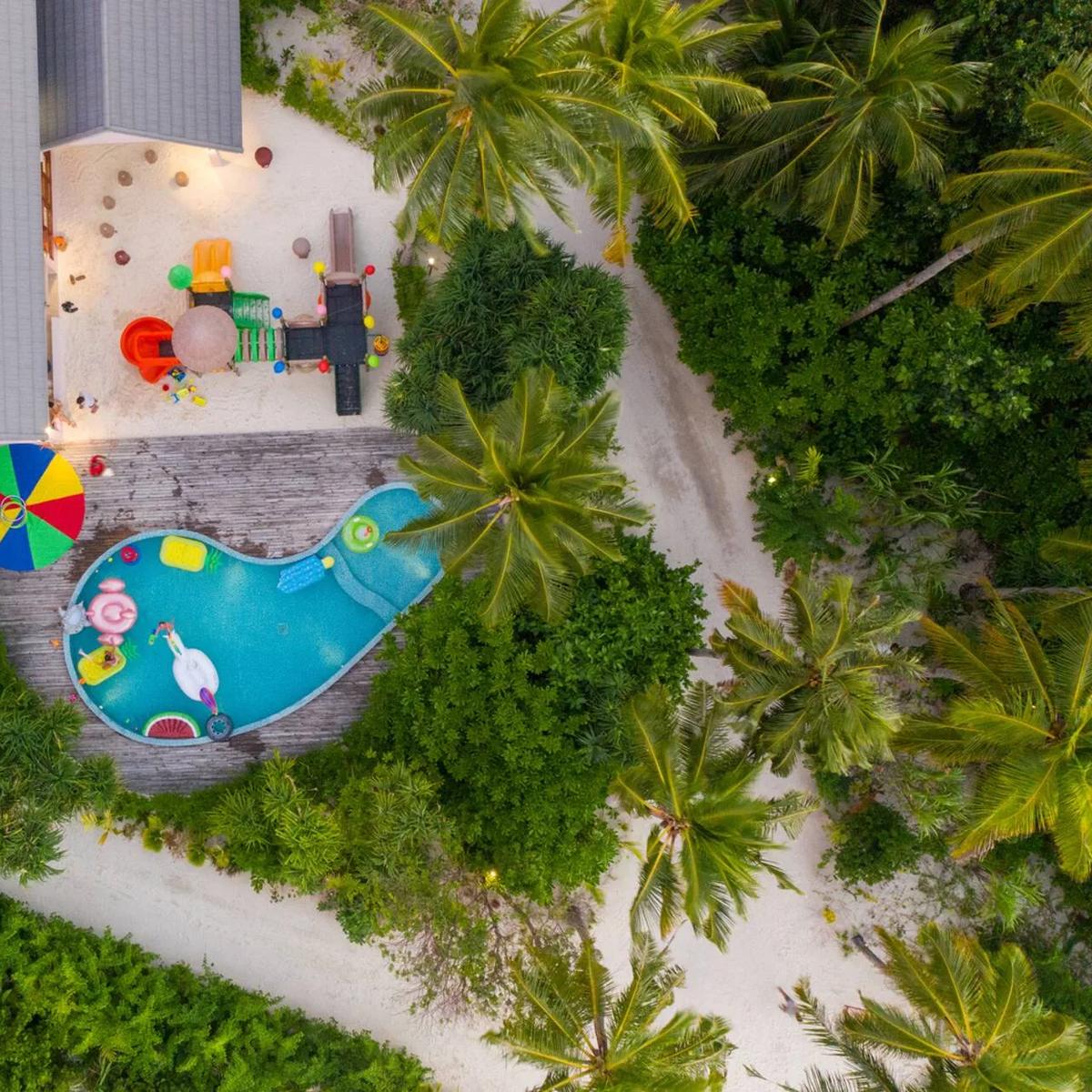 Aerial view of Lil' Shark Kids Club's whale-shaped splash pool and playground, set among palm trees