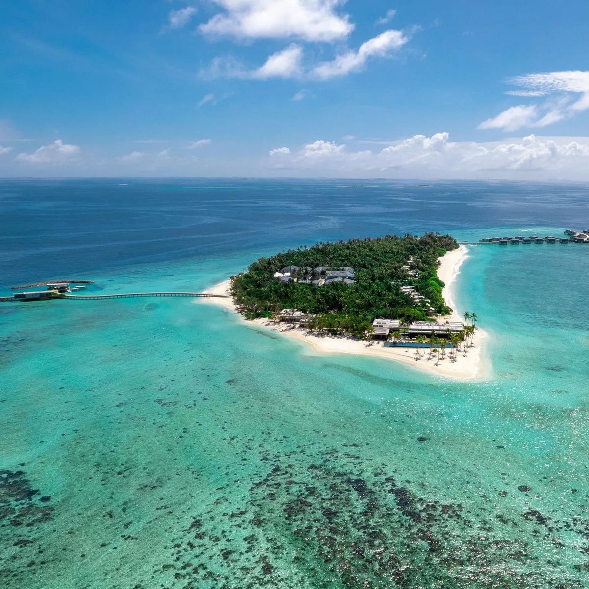 Alila Kothaifaru's island in Raa Atoll seen from the side, dense greenery and beach villas giving way to a row of overwater villas along the reef edge
