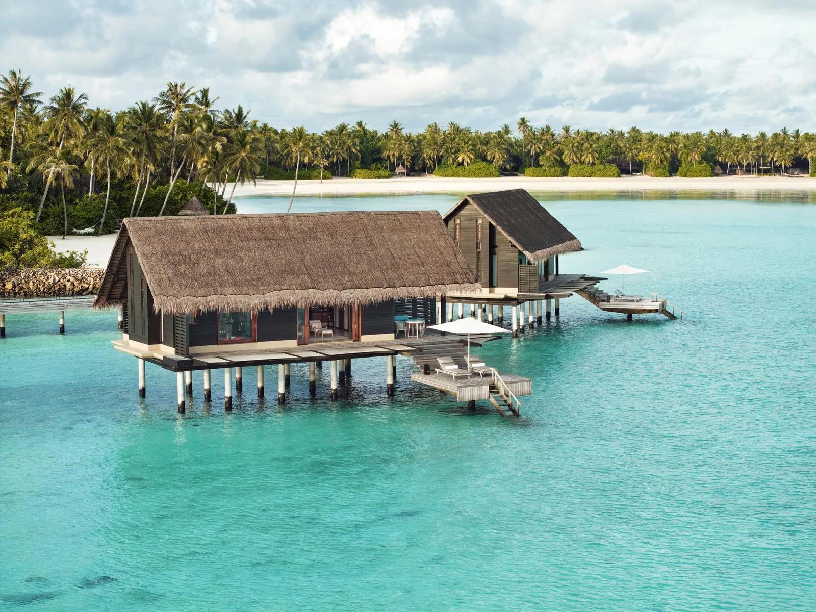 Two thatched-roof Water Villas on stilts above the lagoon at One&Only Reethi Rah, connected by a boardwalk from the beach