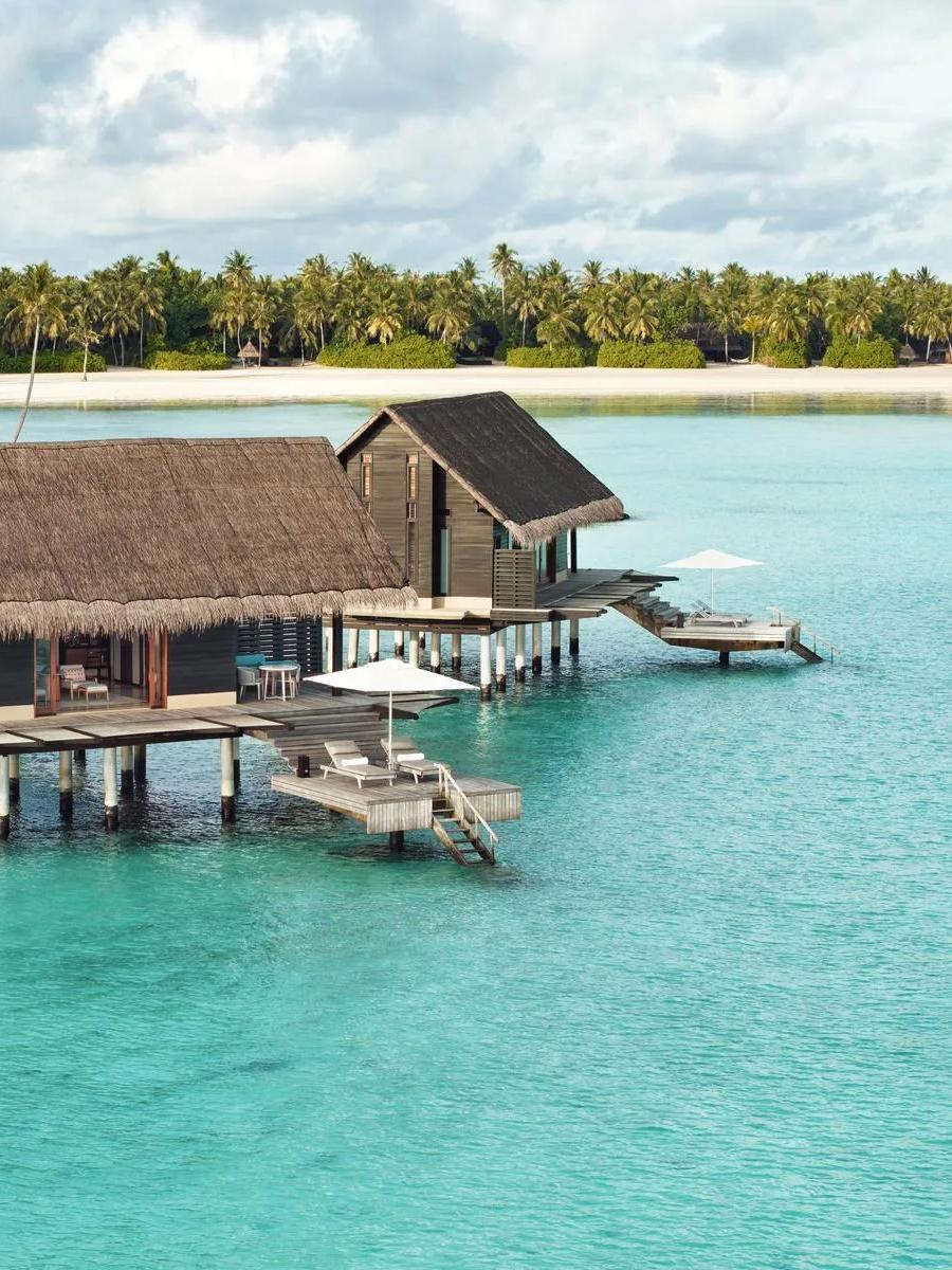 Two thatched-roof Water Villas on stilts above the lagoon at One&Only Reethi Rah, connected by a boardwalk from the beach