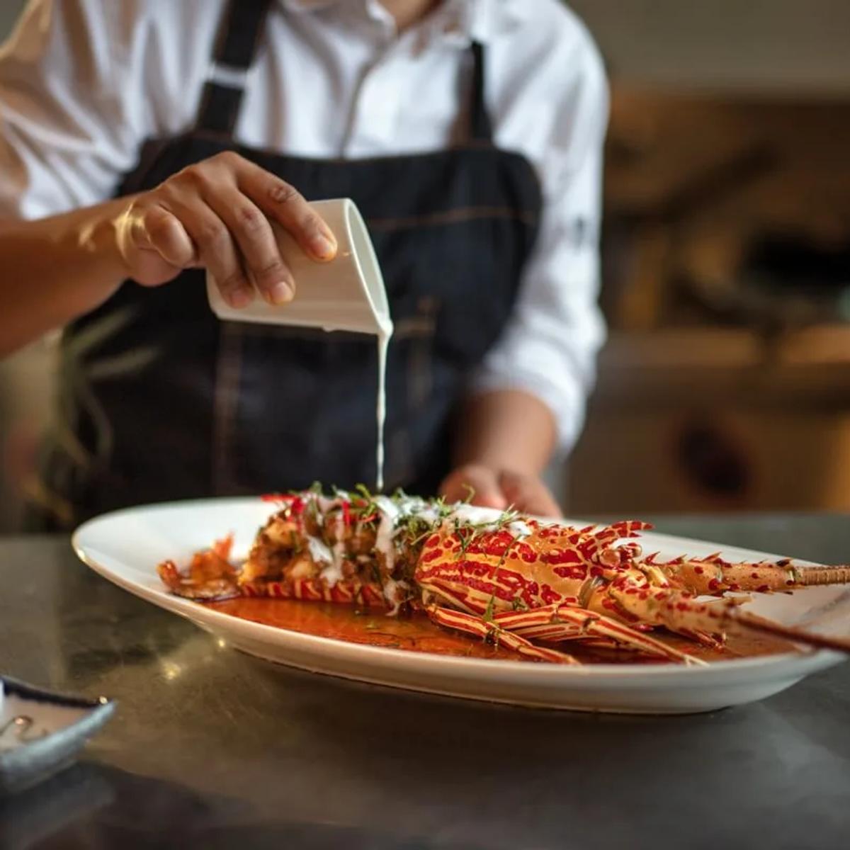 A chef plating a whole grilled lobster at Sea Dragon, Kandima's Far East fine-dining restaurant