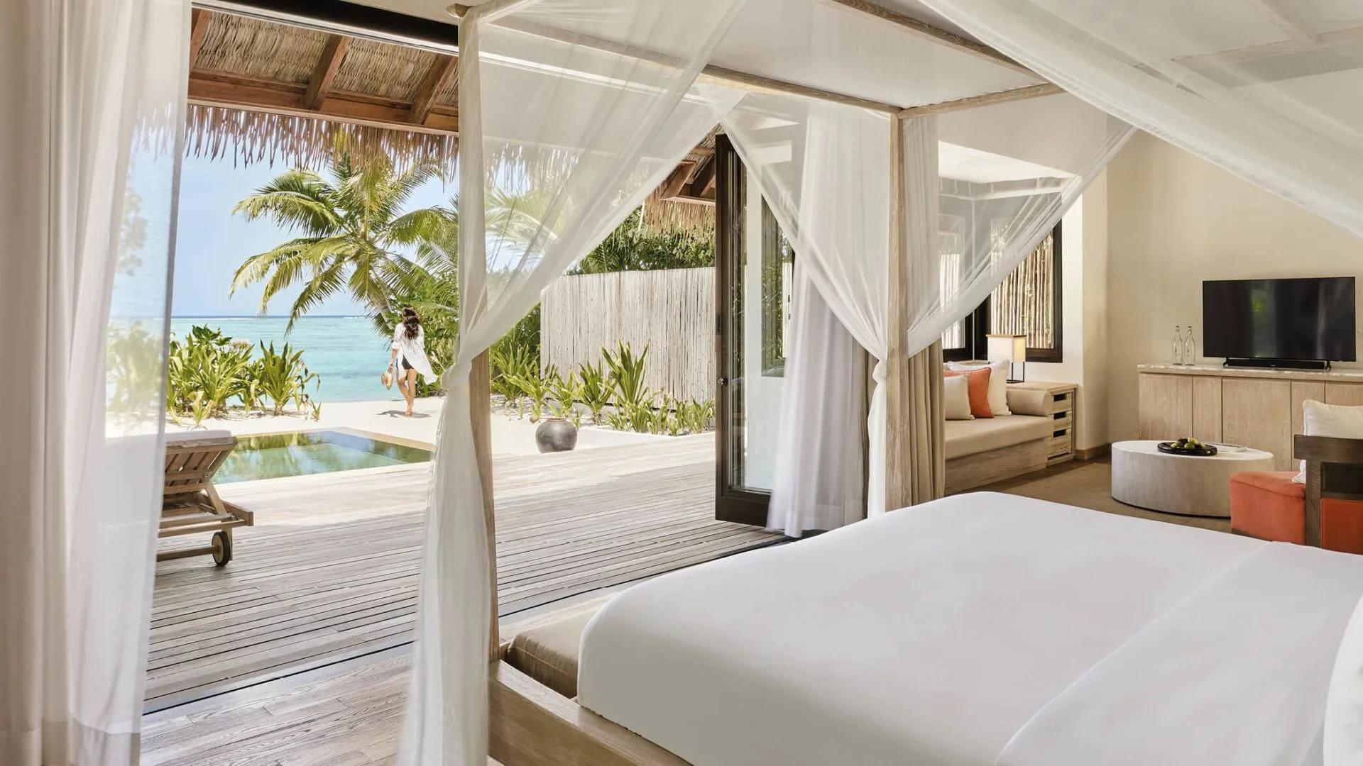 Canopy bed in a Beach Suite bedroom, doors open to a private terrace pool and a palm-lined path to the beach