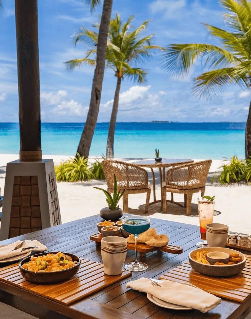 A beachside table set with mezze and drinks, palm trees framing the turquoise ocean beyond