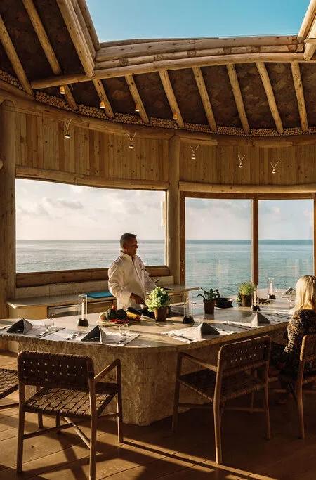 The interior of Once Upon a Table, a circular wood-beamed dining room with floor-to-ceiling ocean views and a single table set for private dining