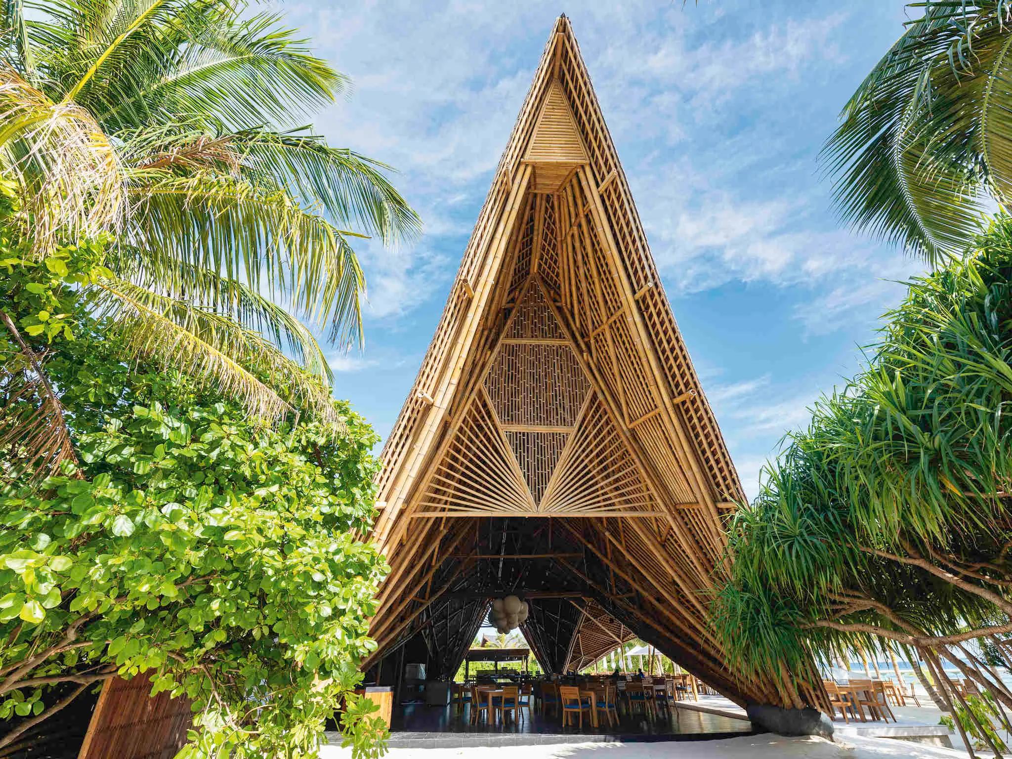 The triangular bamboo roof of ONU Marché rising above palm trees, its peaked lattice structure framed against a blue sky