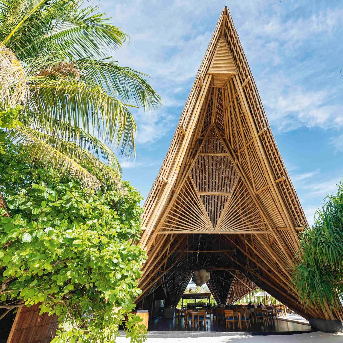 The triangular bamboo roof of ONU Marché rising above palm trees, its peaked lattice structure framed against a blue sky