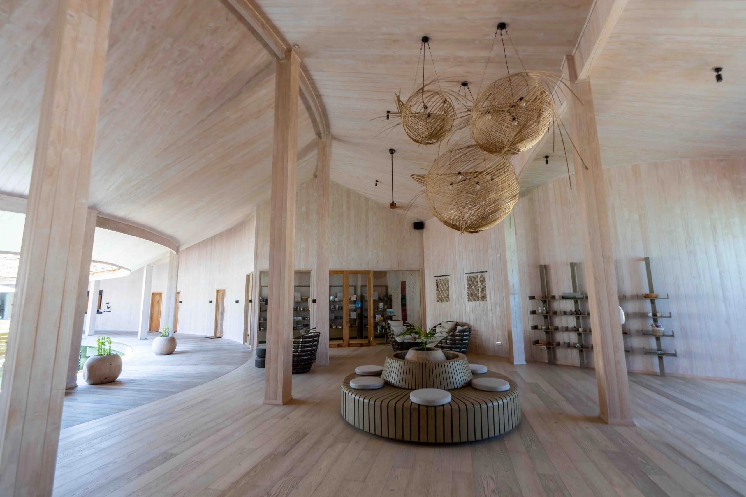 Baani Spa's reception area, a woven straw pendant light hanging over a curved wooden bench and shelving of spa products