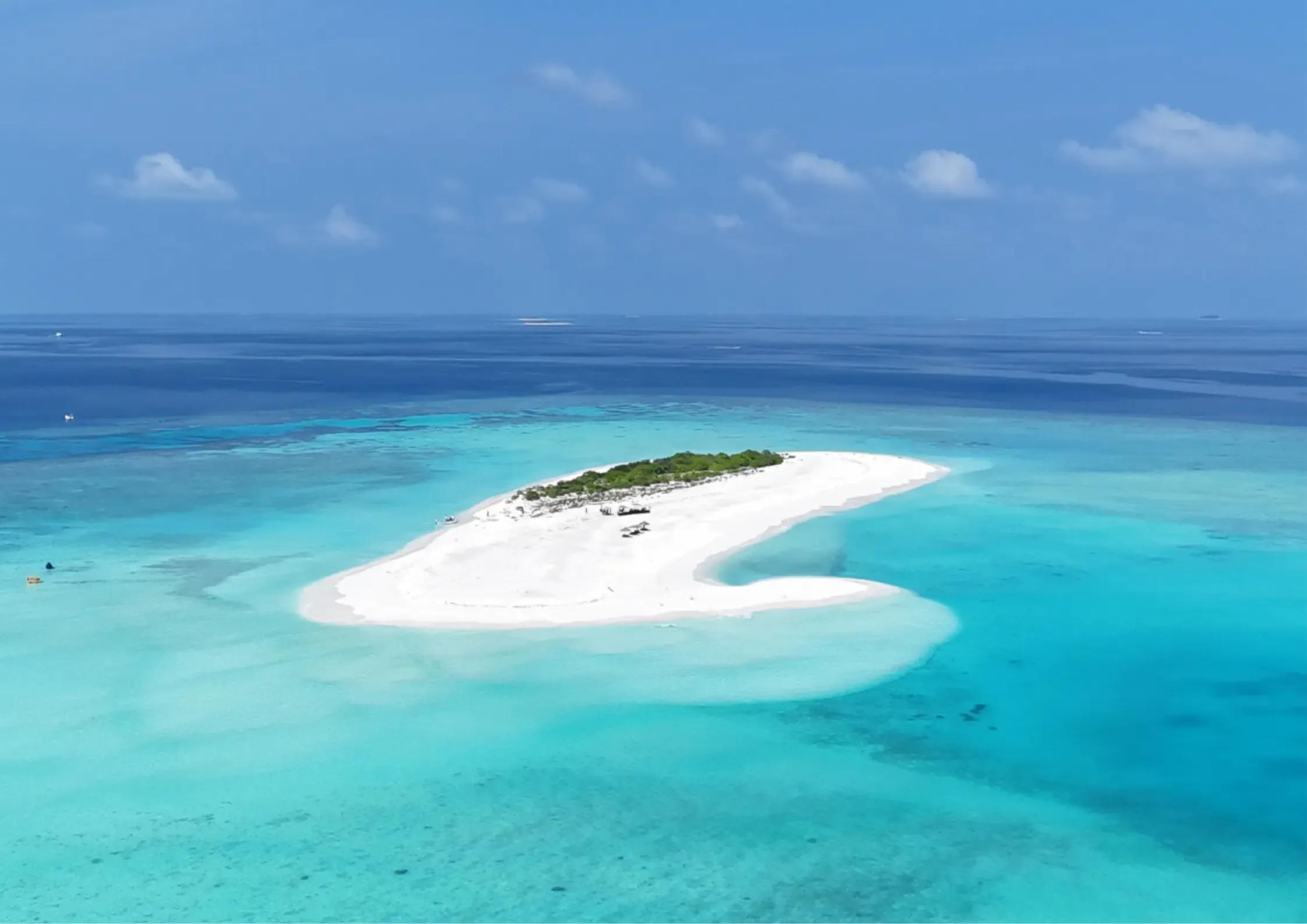Aerial view of an uninhabited sandbank near Niva Dhigali, reef shading from pale turquoise to deep blue