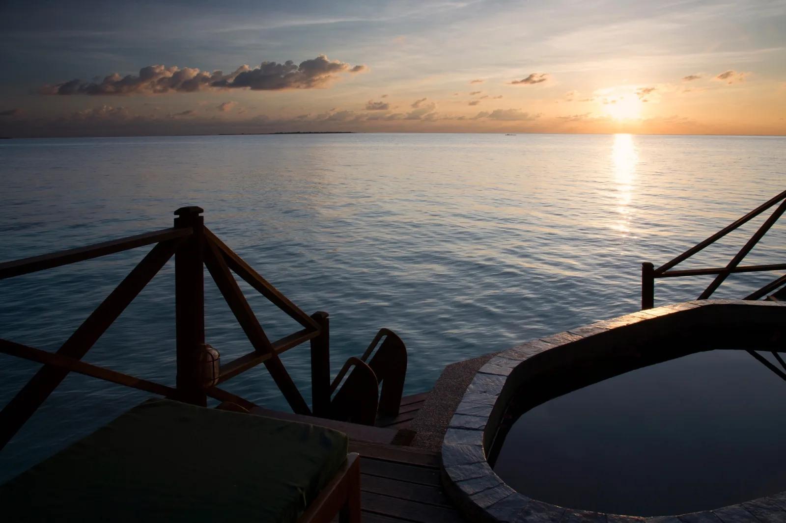 A private plunge pool on an overwater villa deck at dusk, looking out over open water toward the horizon