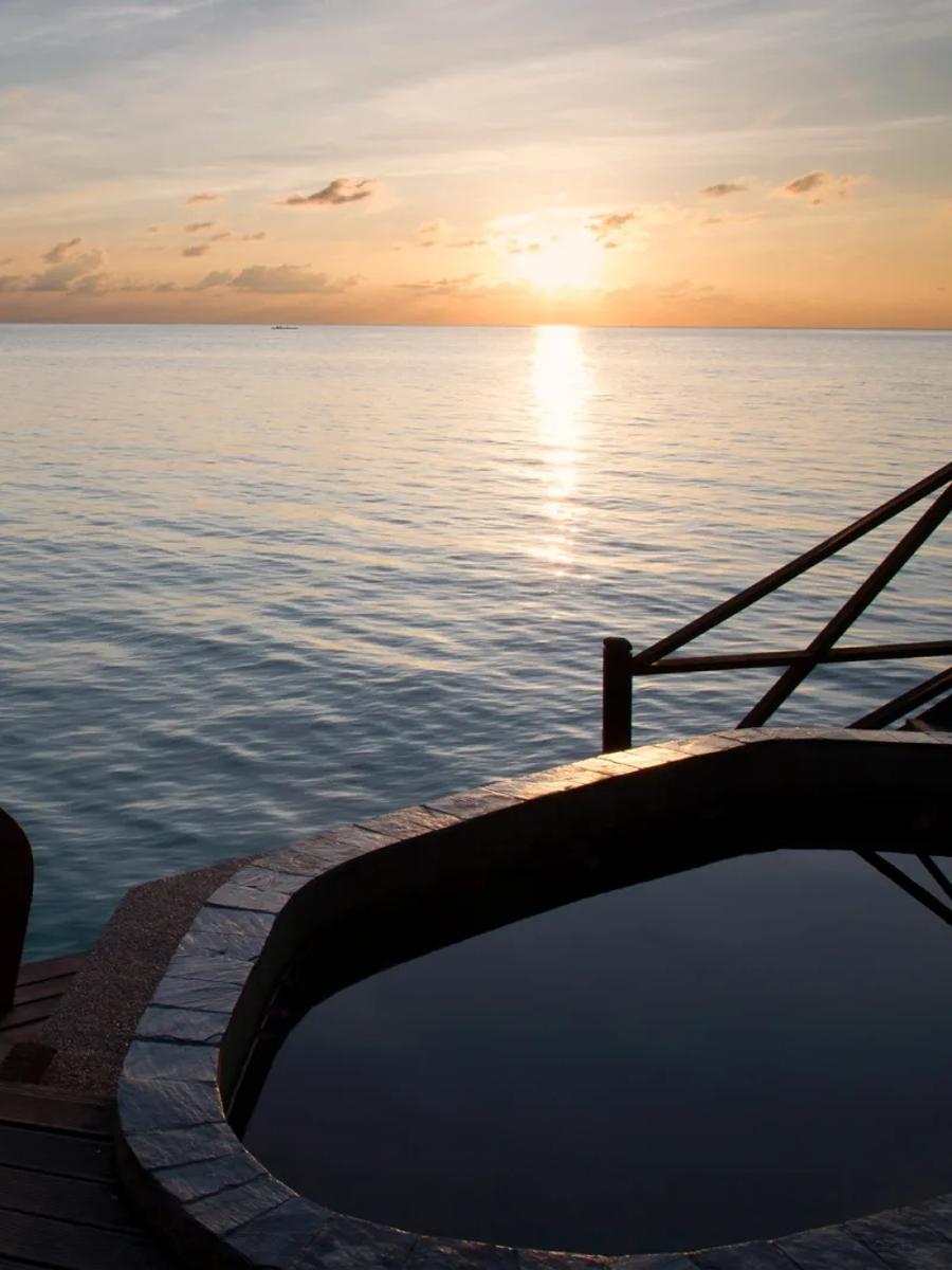 A private plunge pool on an overwater villa deck at dusk, looking out over open water toward the horizon