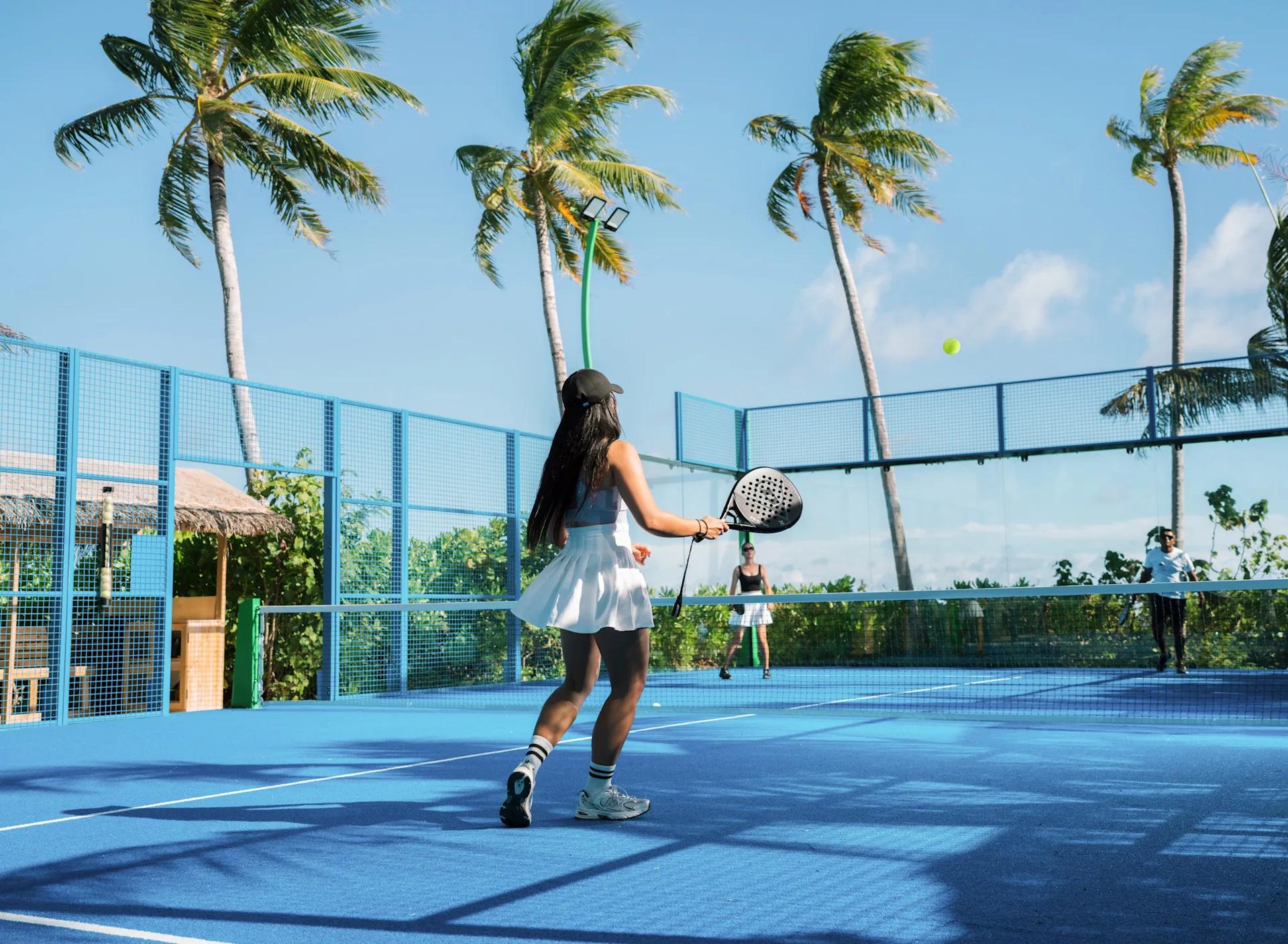 A guest playing padel on the resort's seaside padel court, with a sports animator on hand