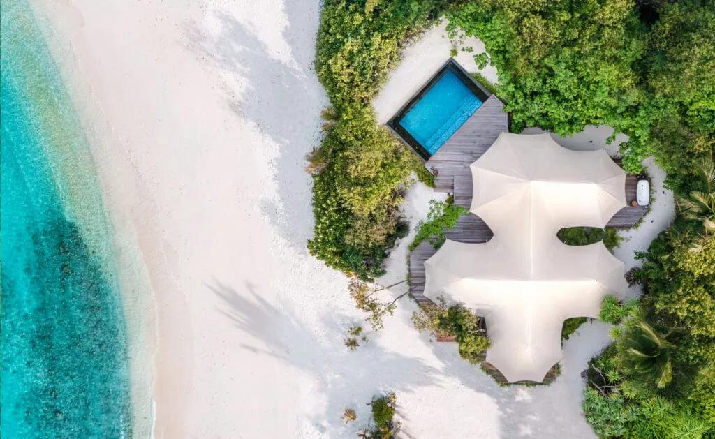 Aerial view of a tented villa's canvas roof and private pool deck, set into the sand among trees