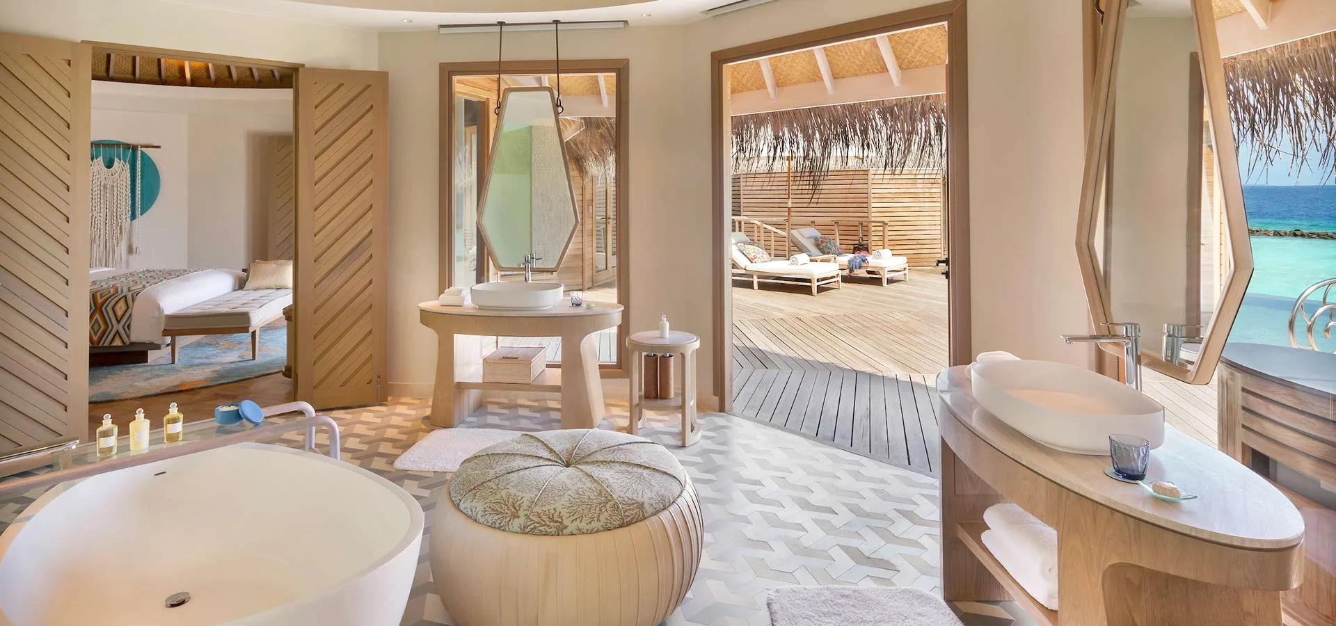 An Ocean House bathroom with a freestanding tub, opening directly onto the villa's overwater deck and loungers.