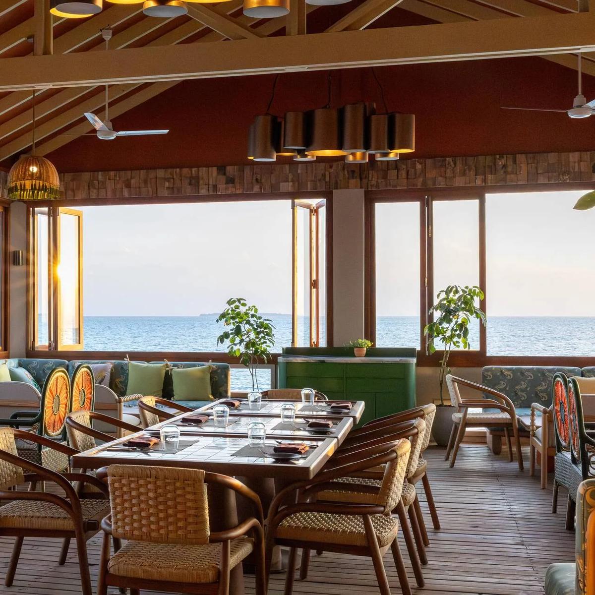 Onda's open-air overwater dining room at The Standard, tables and lounge seating set toward the ocean at sunset