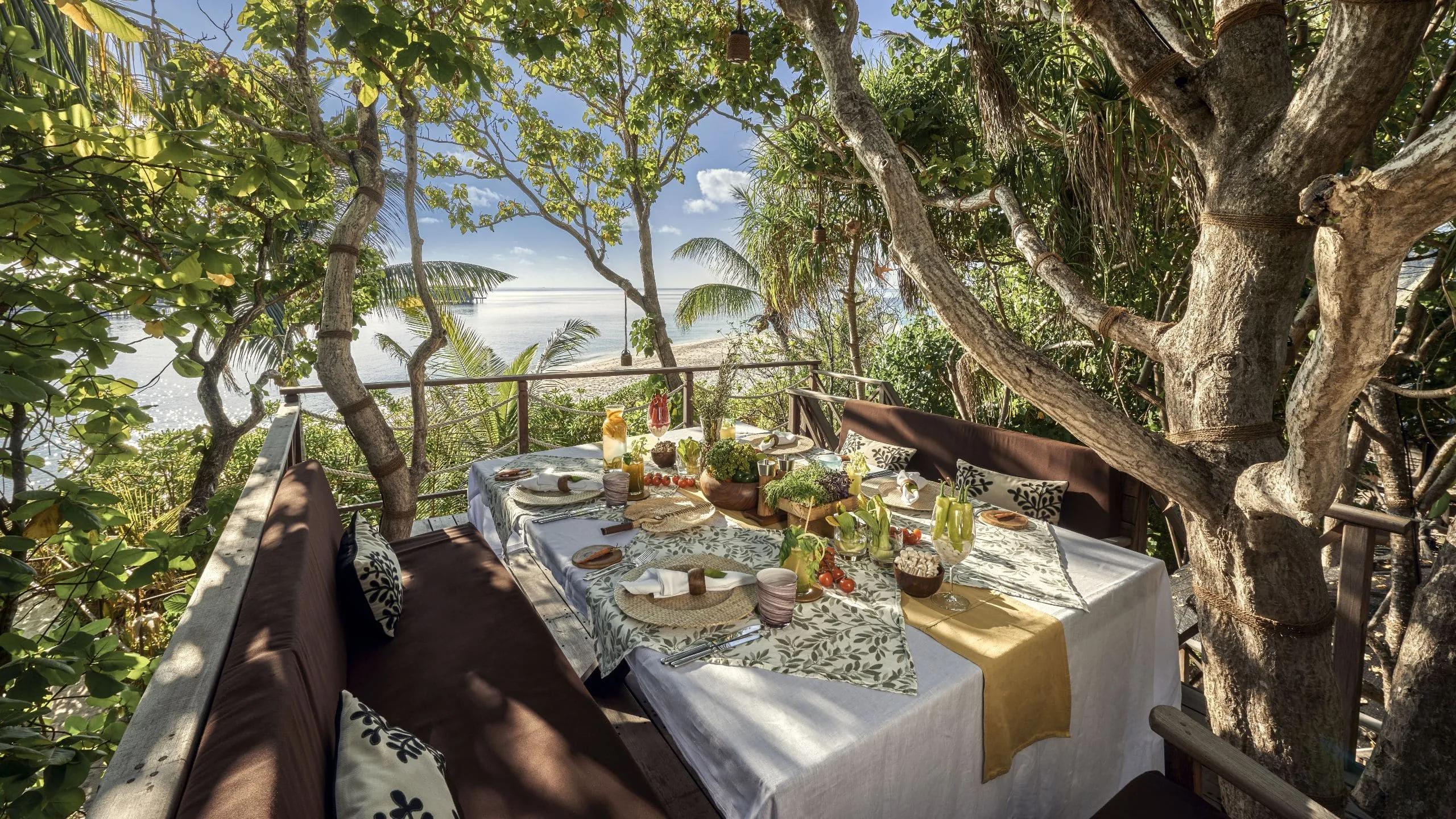 A table set on the elevated deck of Chef's Garden Treehouse, looking out through the trees to the beach