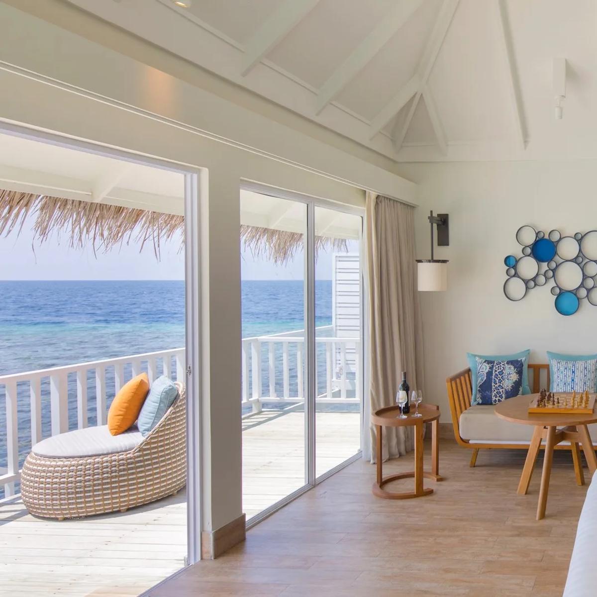 The living area of a Family Overwater Villa, daybed and chess table beside sliding doors onto the lagoon
