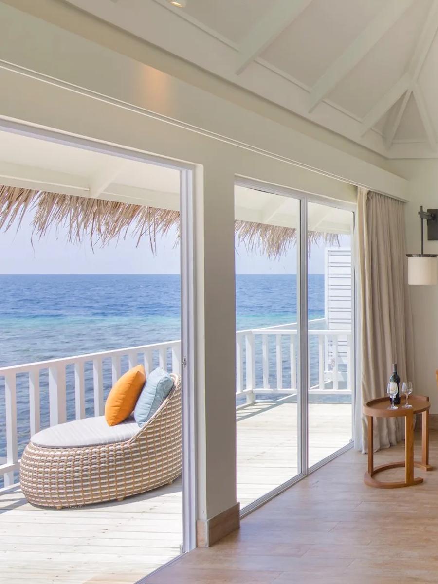 The living area of a Family Overwater Villa, daybed and chess table beside sliding doors onto the lagoon