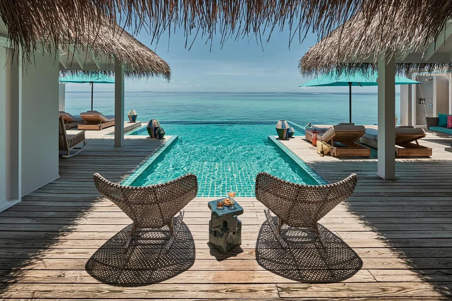 A Two Bedroom Rockstar Villa's overwater deck, framed by thatched roof eaves, with a plunge pool running to an infinity edge over open ocean