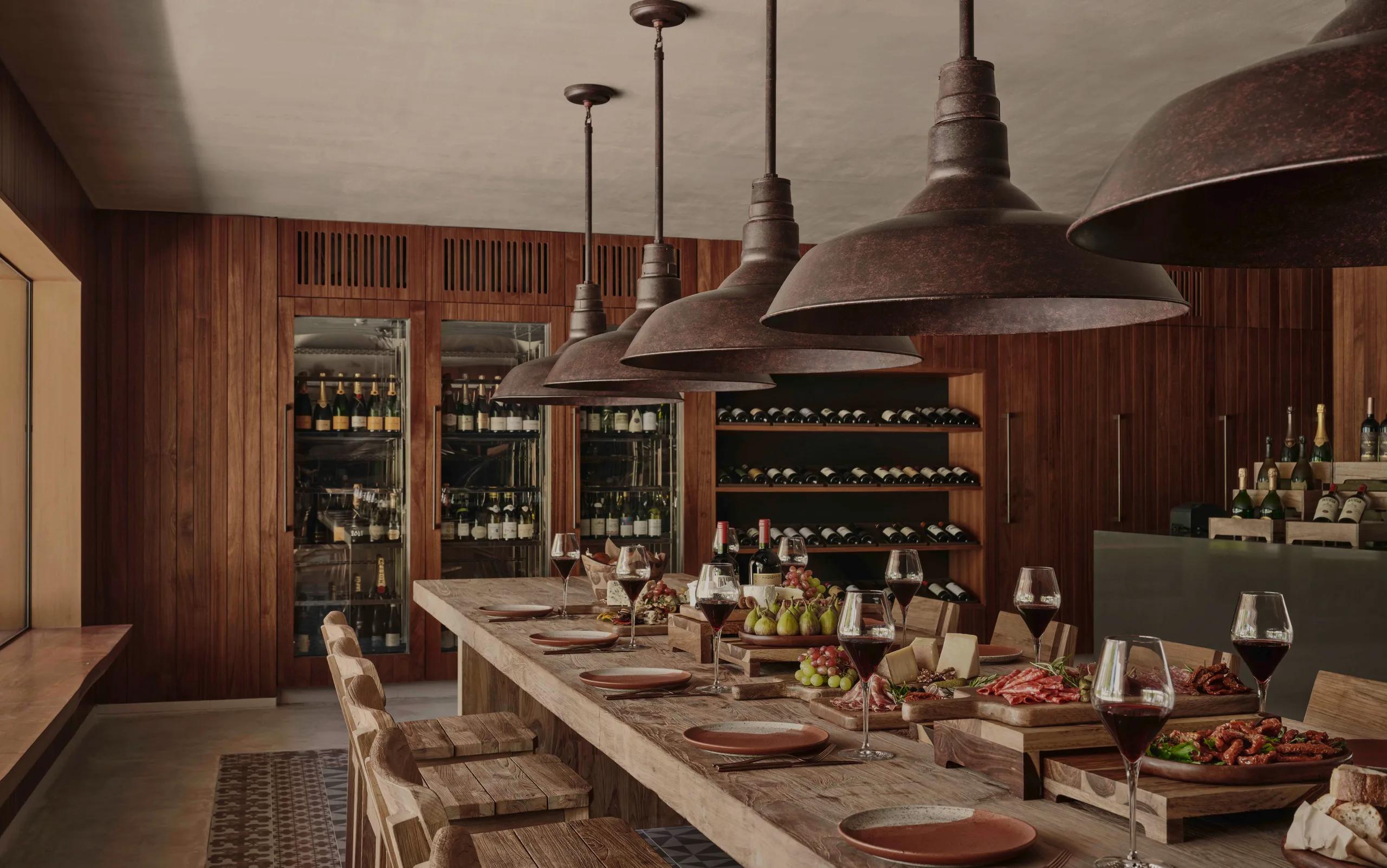 A long wooden tasting table set with charcuterie, cheese, and wine at Farine, shelves of bottles lining the room