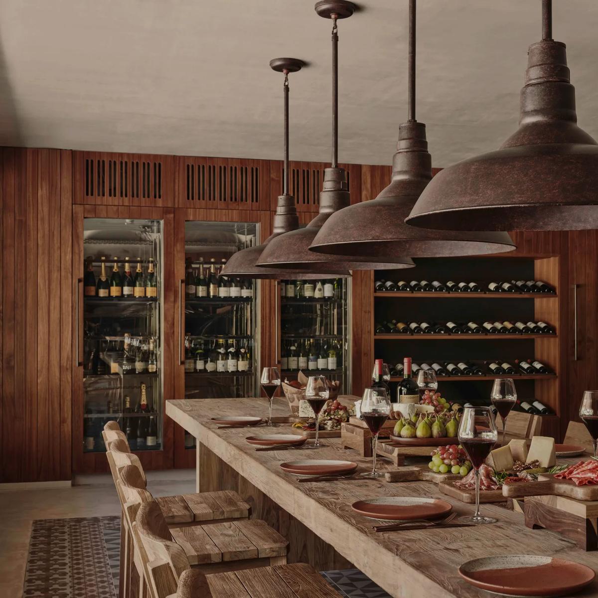 A long wooden tasting table set with charcuterie, cheese, and wine at Farine, shelves of bottles lining the room