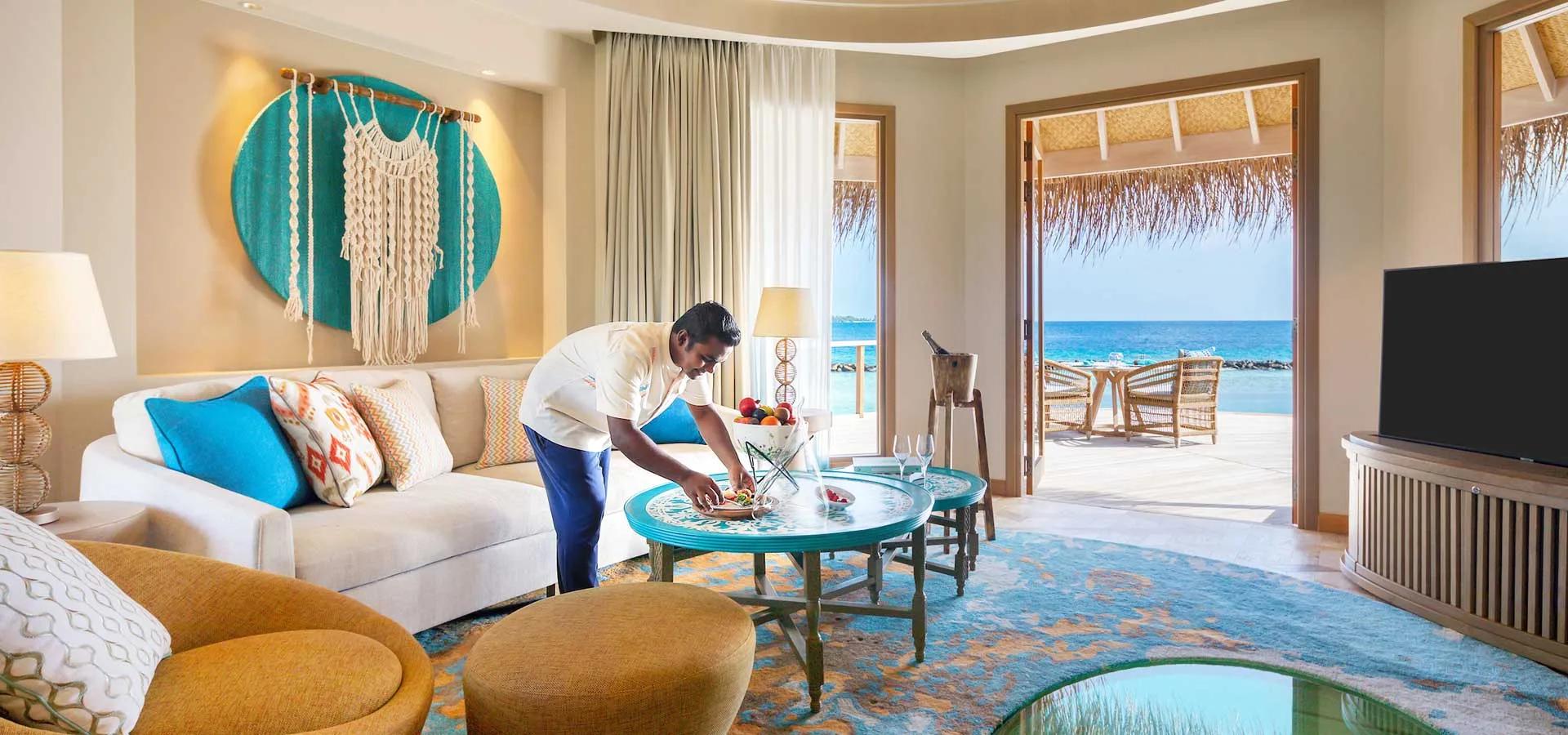 An Ocean House living room, its butler arranging a bowl of fruit beside sofas that open onto the overwater deck.
