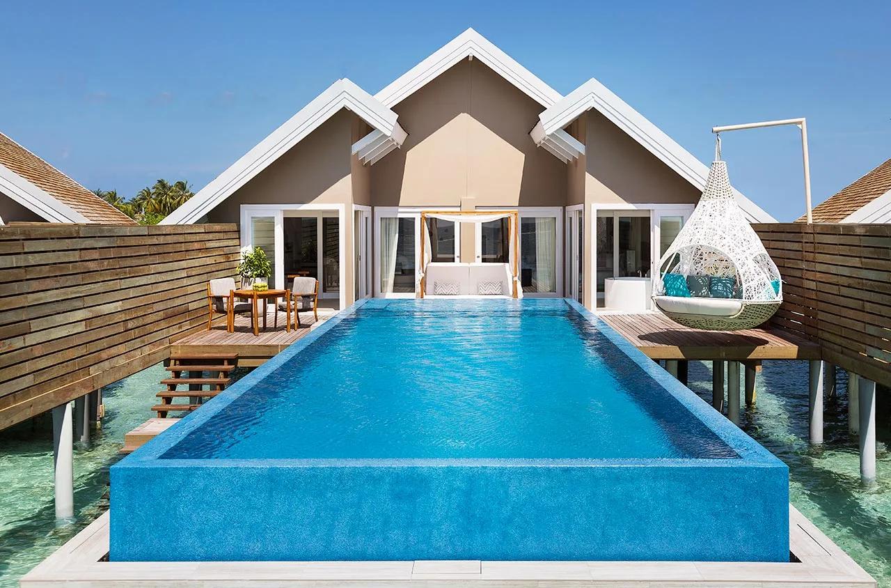 An overwater Temptation Pool Water Villa with its private pool under full sun, the villa row visible beyond