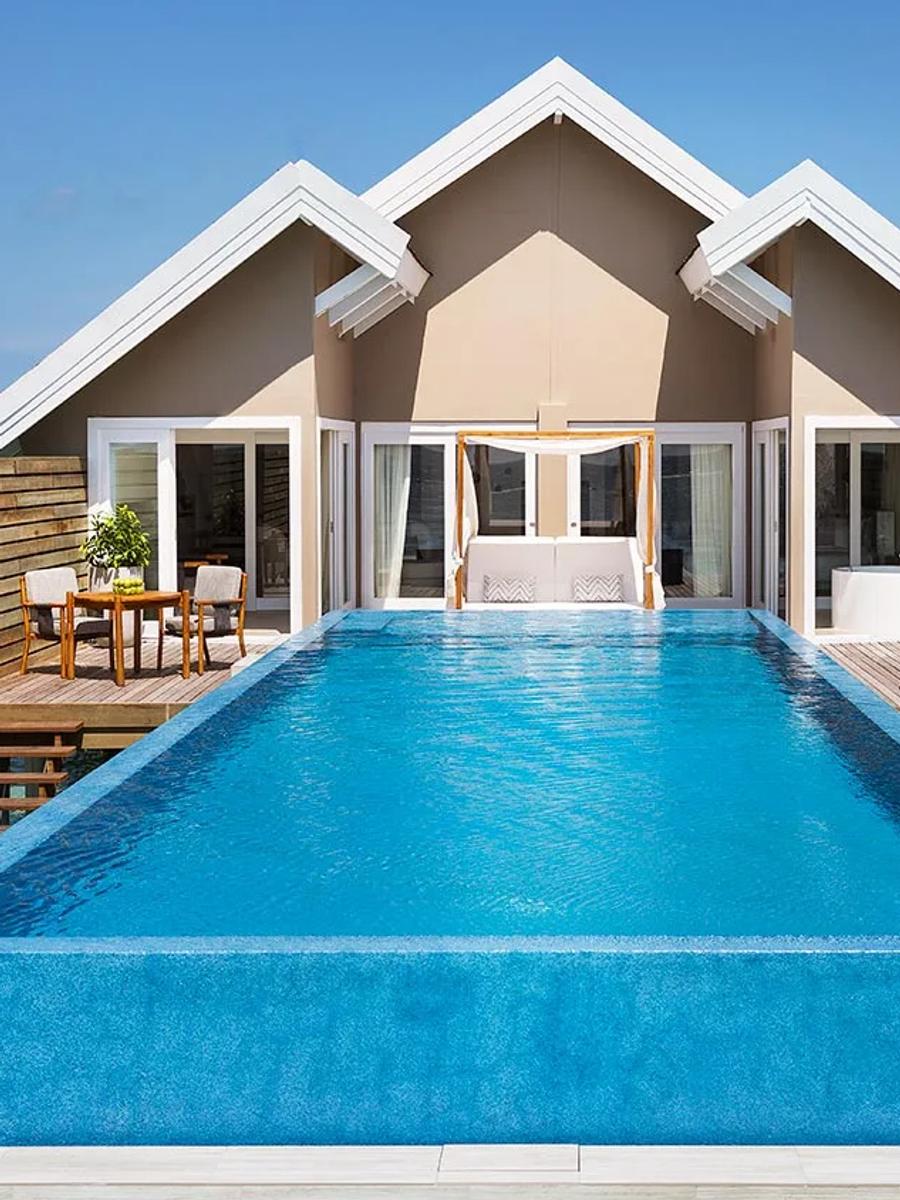 An overwater Temptation Pool Water Villa with its private pool under full sun, the villa row visible beyond