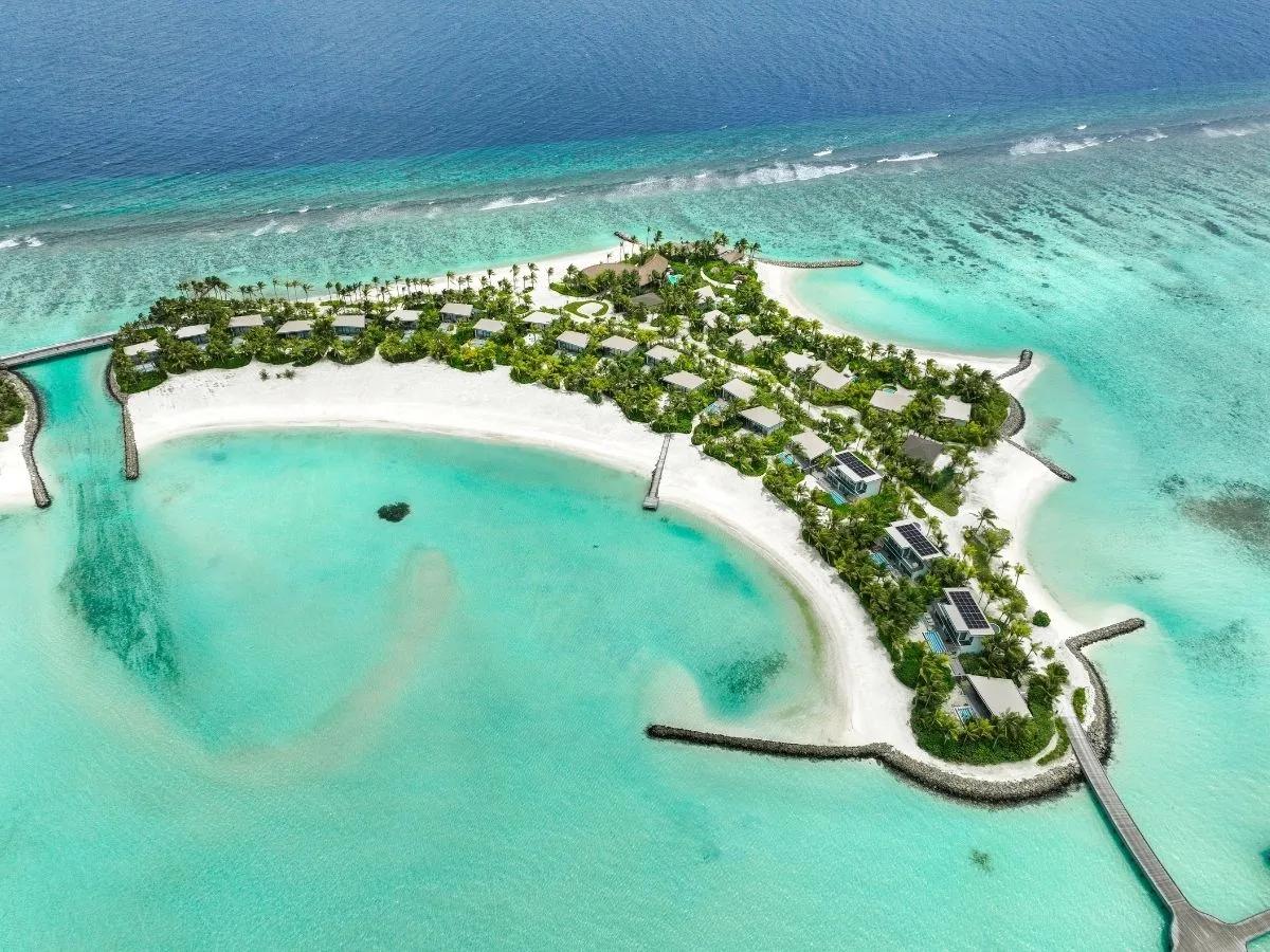Aerial view of SO/ Maldives' curved beach and palm-screened villas wrapped around a shallow lagoon