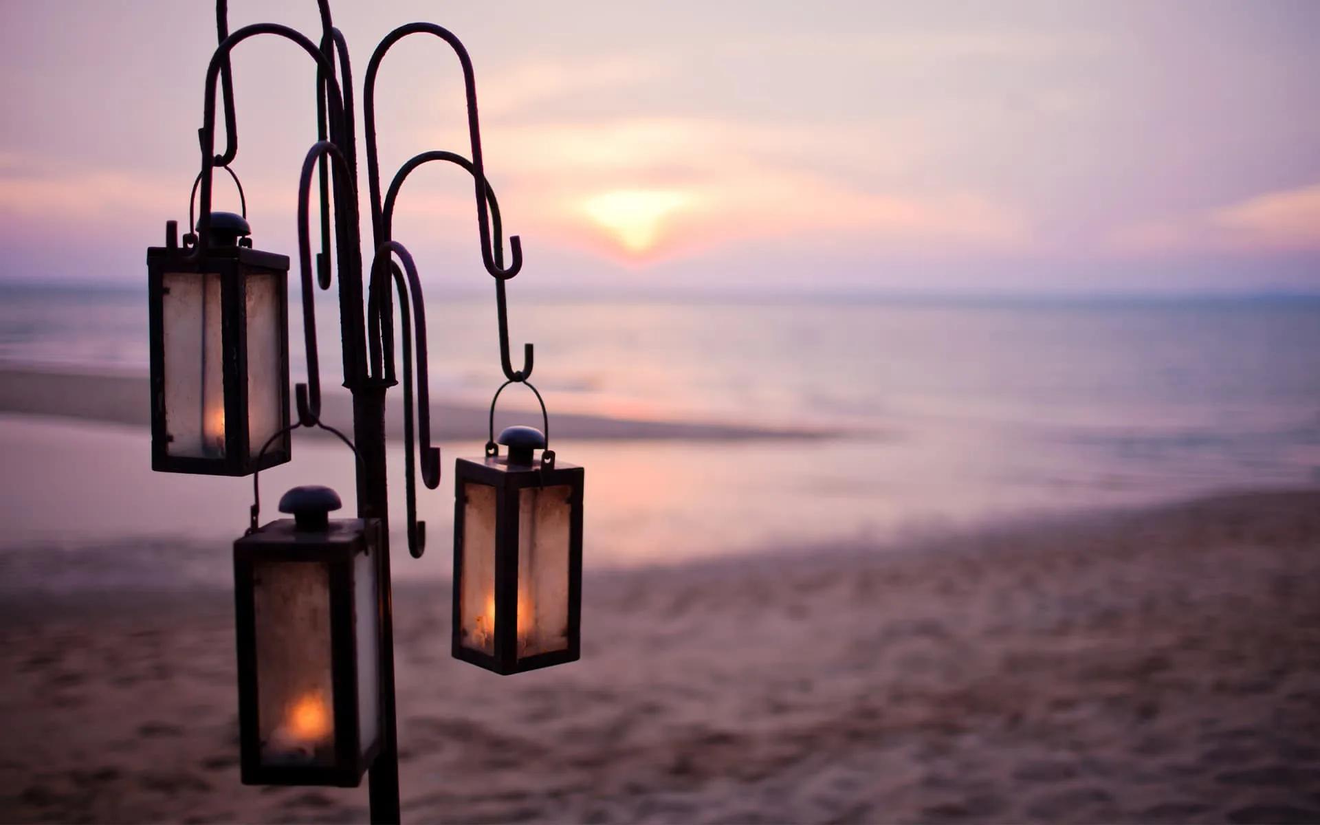 A private dining setup of hanging lanterns on the beach at dusk
