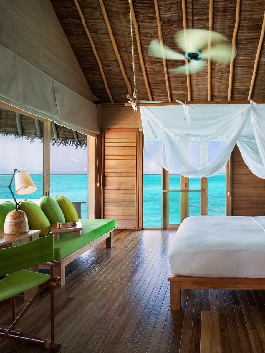 A bedroom in an overwater villa with a sheer canopy over the bed and glass doors opening onto the lagoon