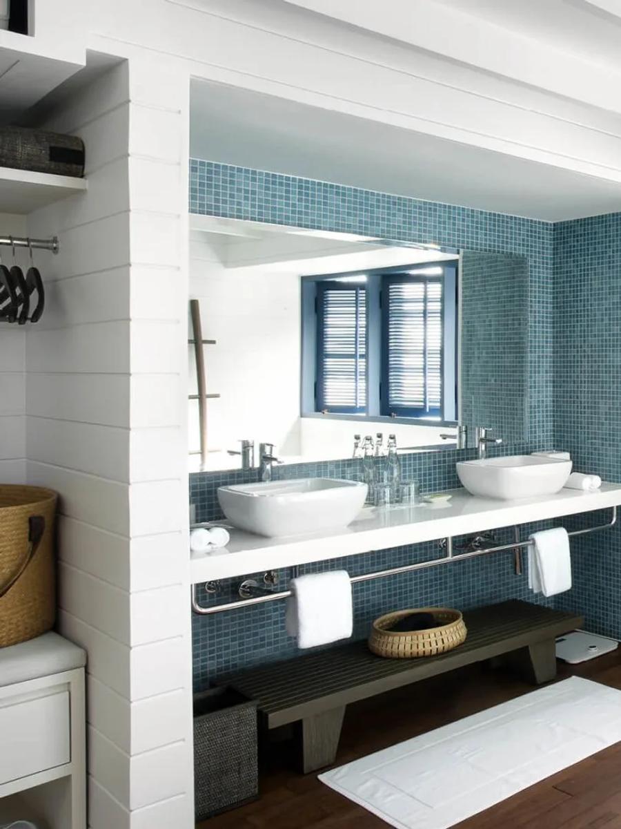 The bathroom of a Dhoni Loft Water Villa, with a freestanding tub set beneath tall blue-shuttered windows