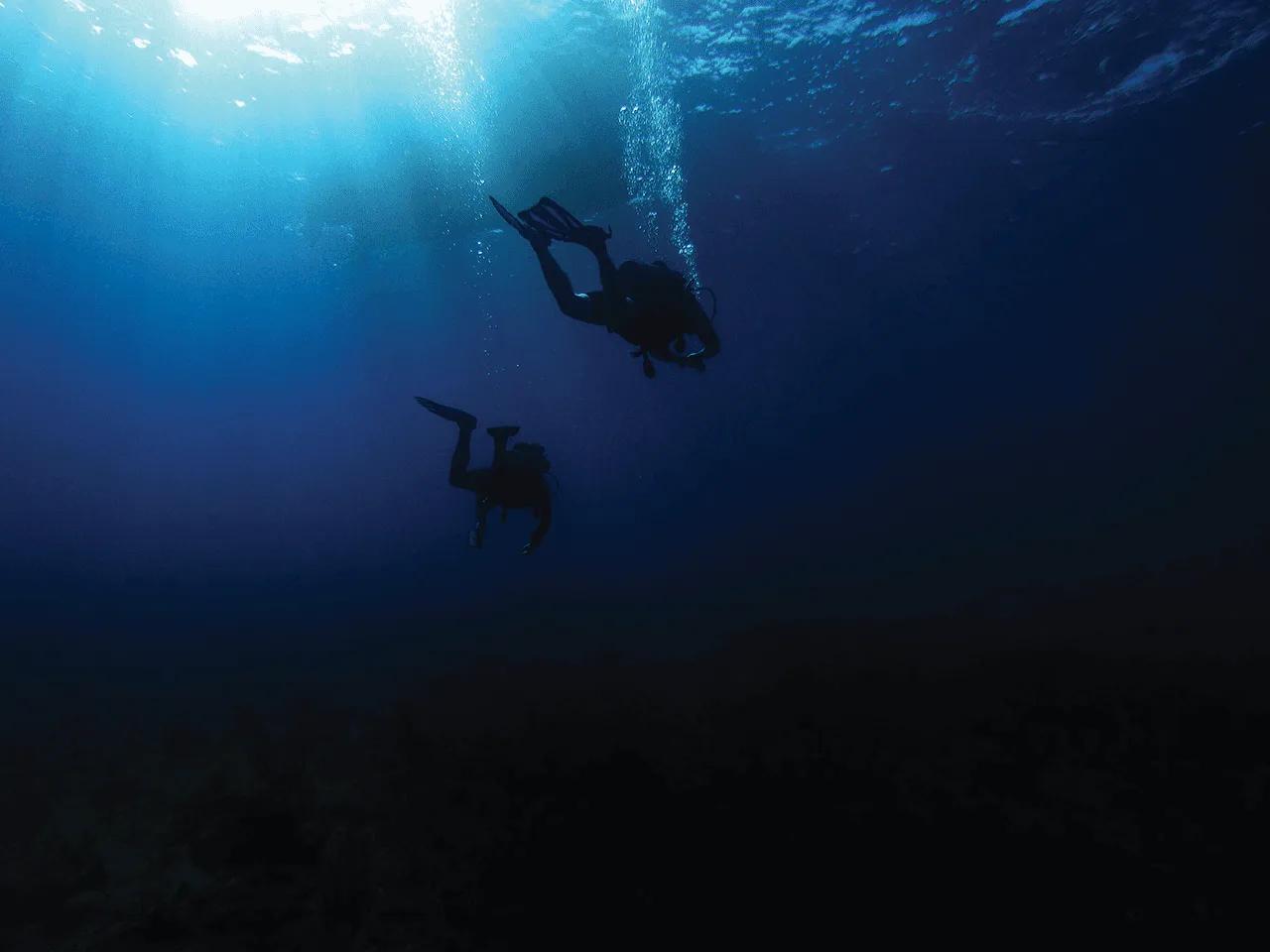 Two scuba divers descending through sunlit water toward the reef