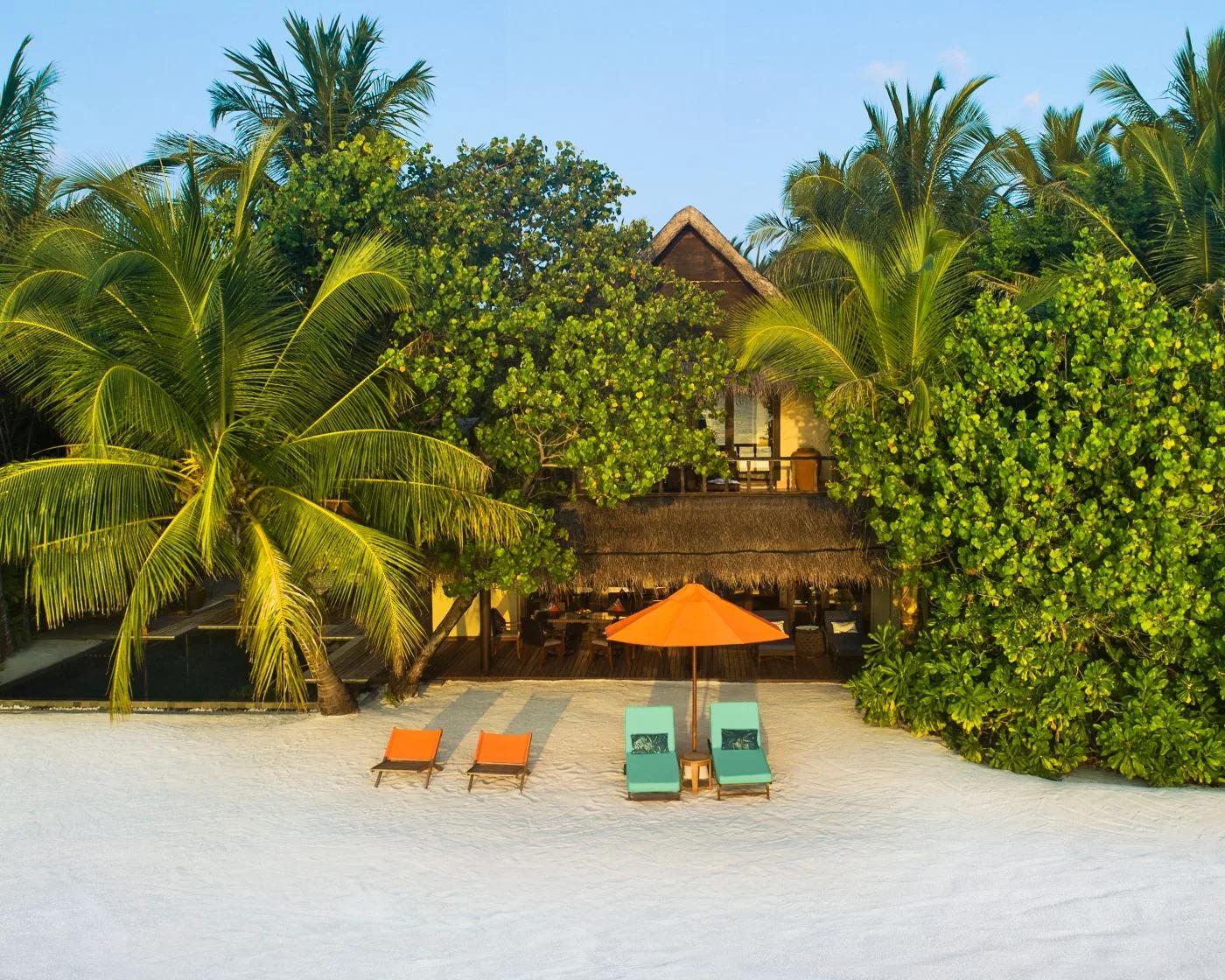 A Two Bedroom Sunset Beachfront Suite with Pool at golden hour, sun loungers set on the beach in front of its two storeys