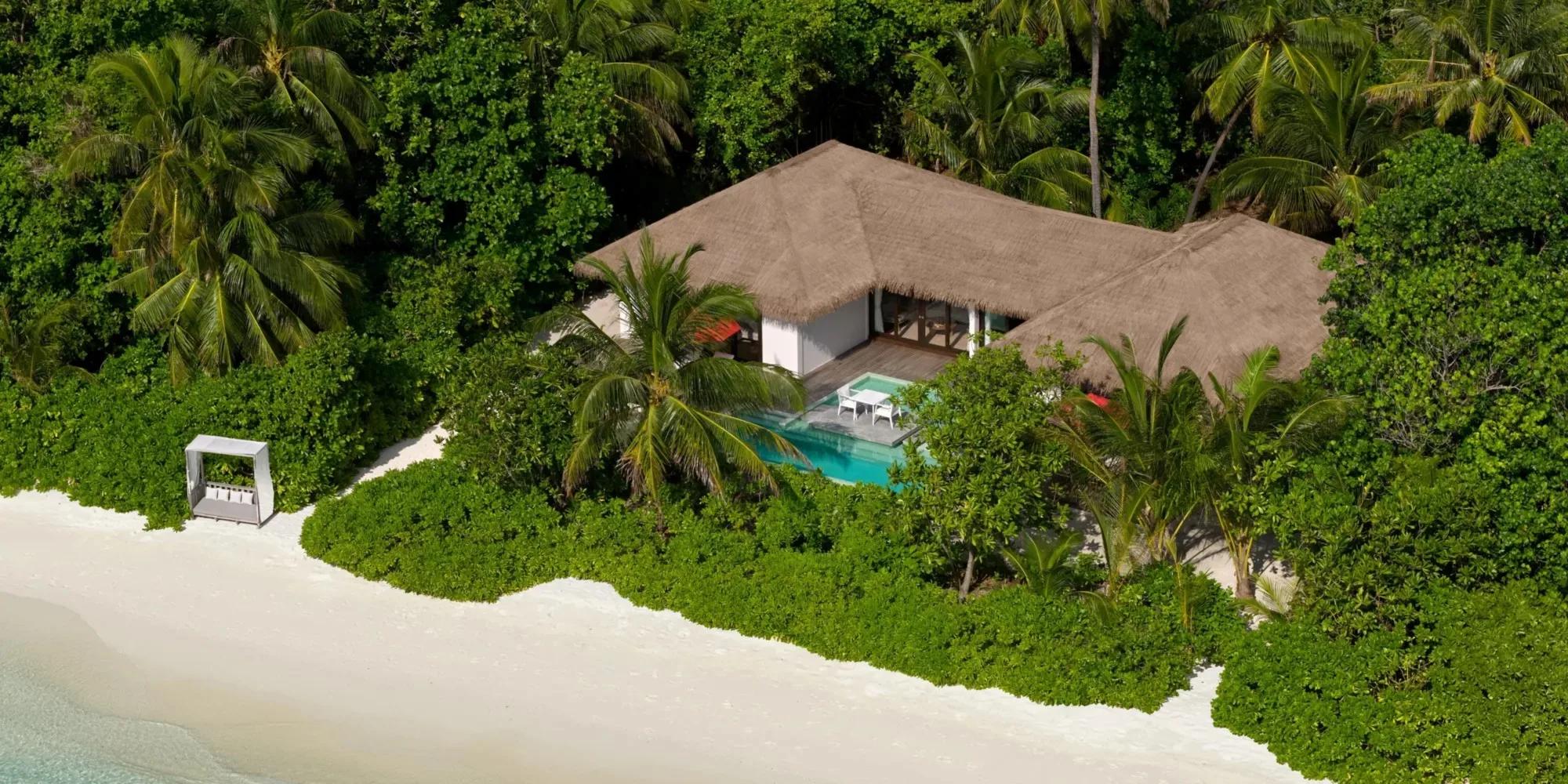 A Beach Villa at Noku Maldives seen from above, its thatched roof and private pool set among palms just off the sand
